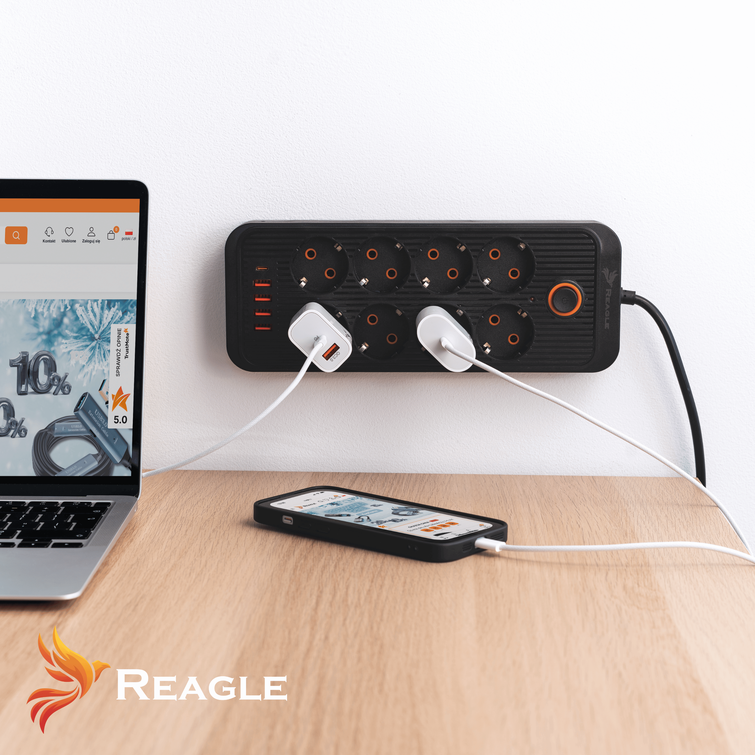 Laptop, telefon i czarna listwa zasilająca z podłączonymi ładowarkami.