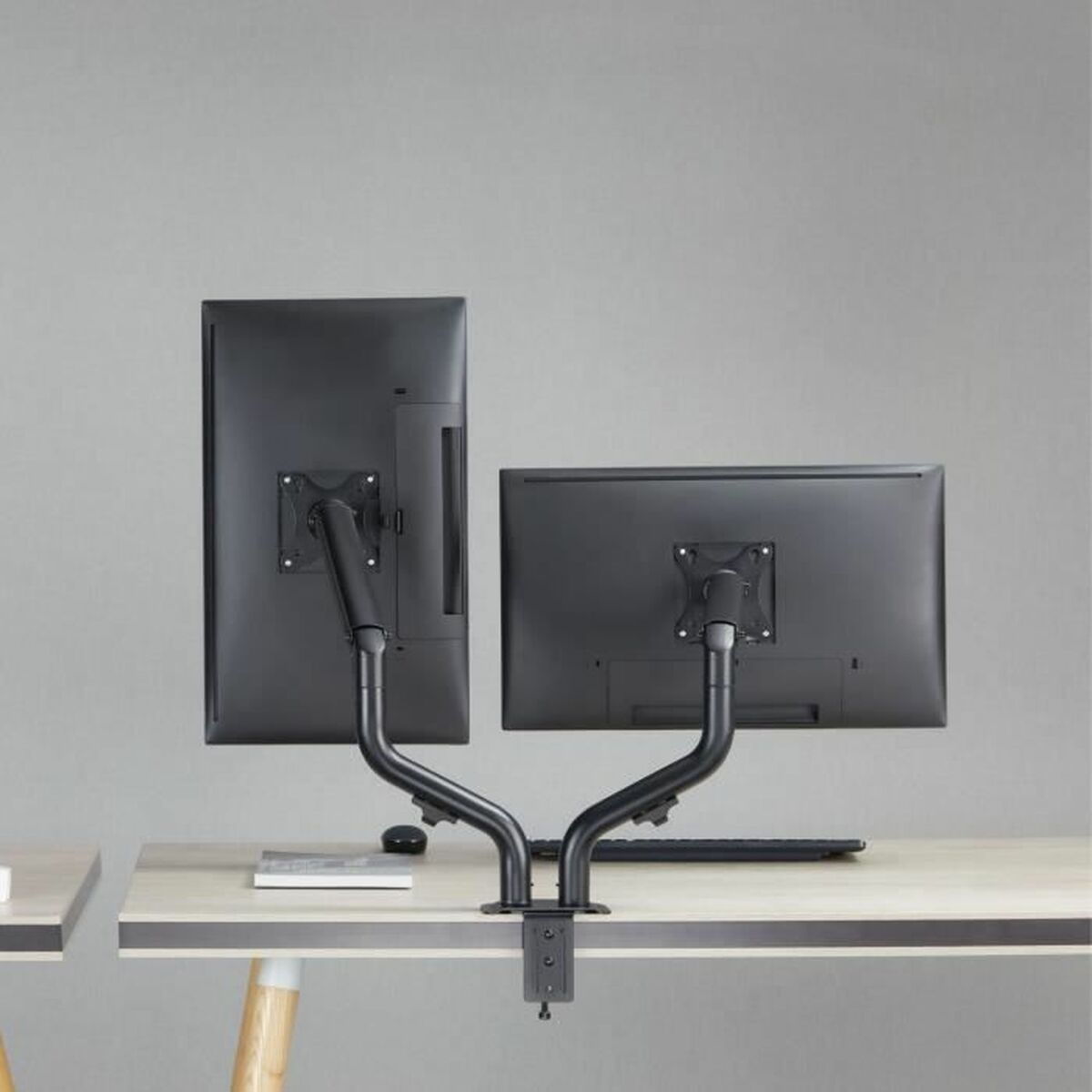 Due monitor neri su una scrivania con bracci regolabili su sfondo grigio.