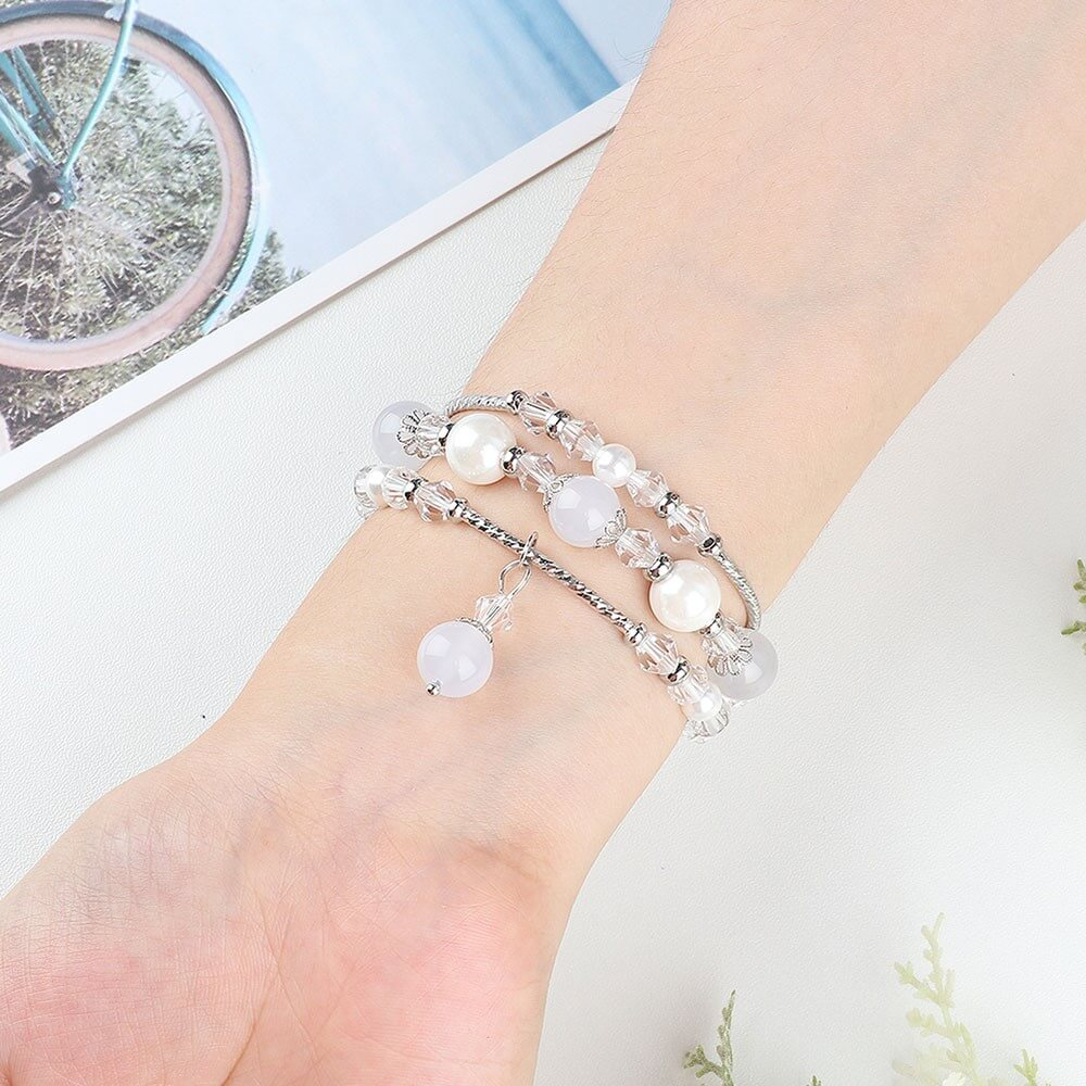 Un bracelet avec des perles blanches et des cristaux clairs autour d'un poignet.