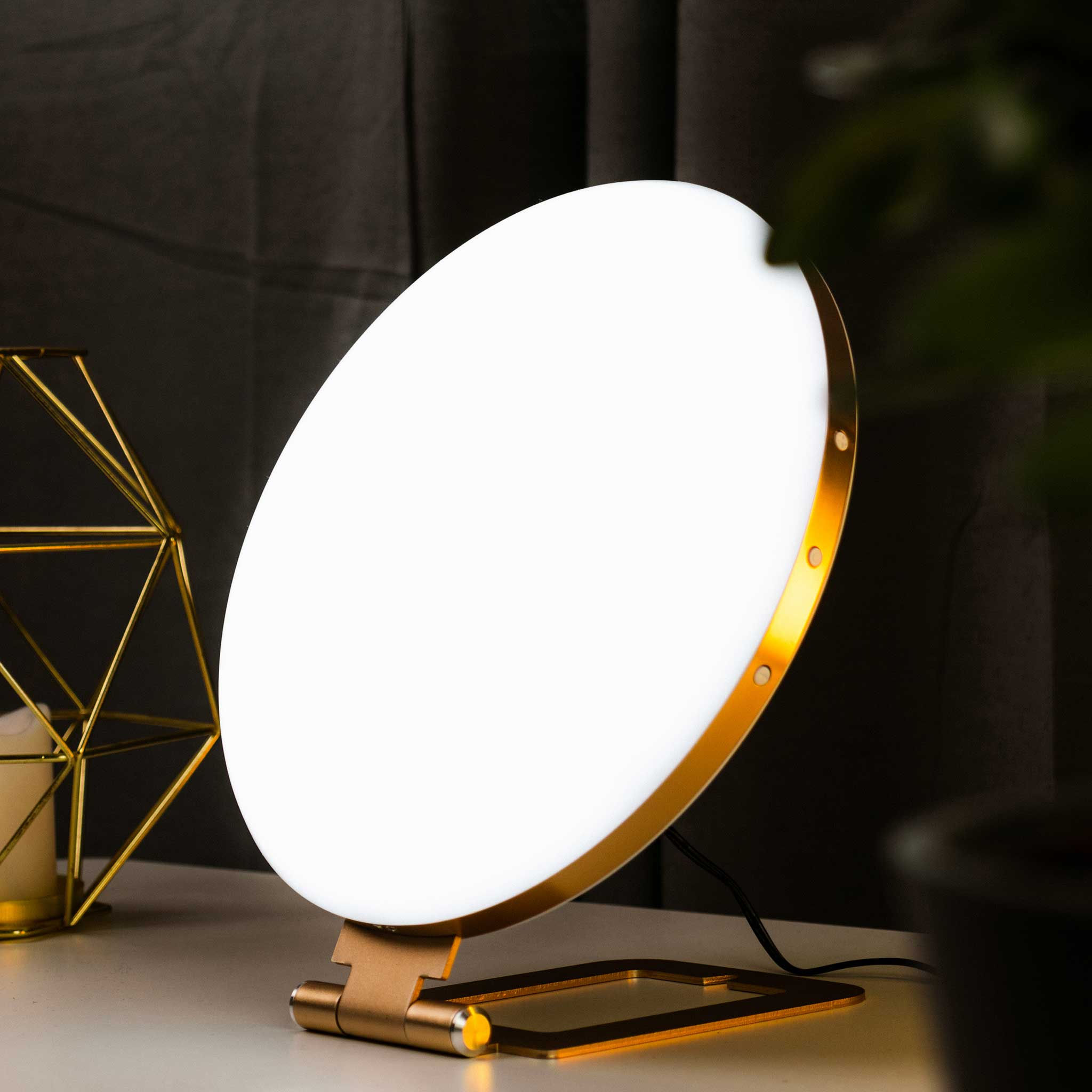 Ein goldener Lichttherapie-Tisch mit runder Lampe vor dunklem Hintergrund.