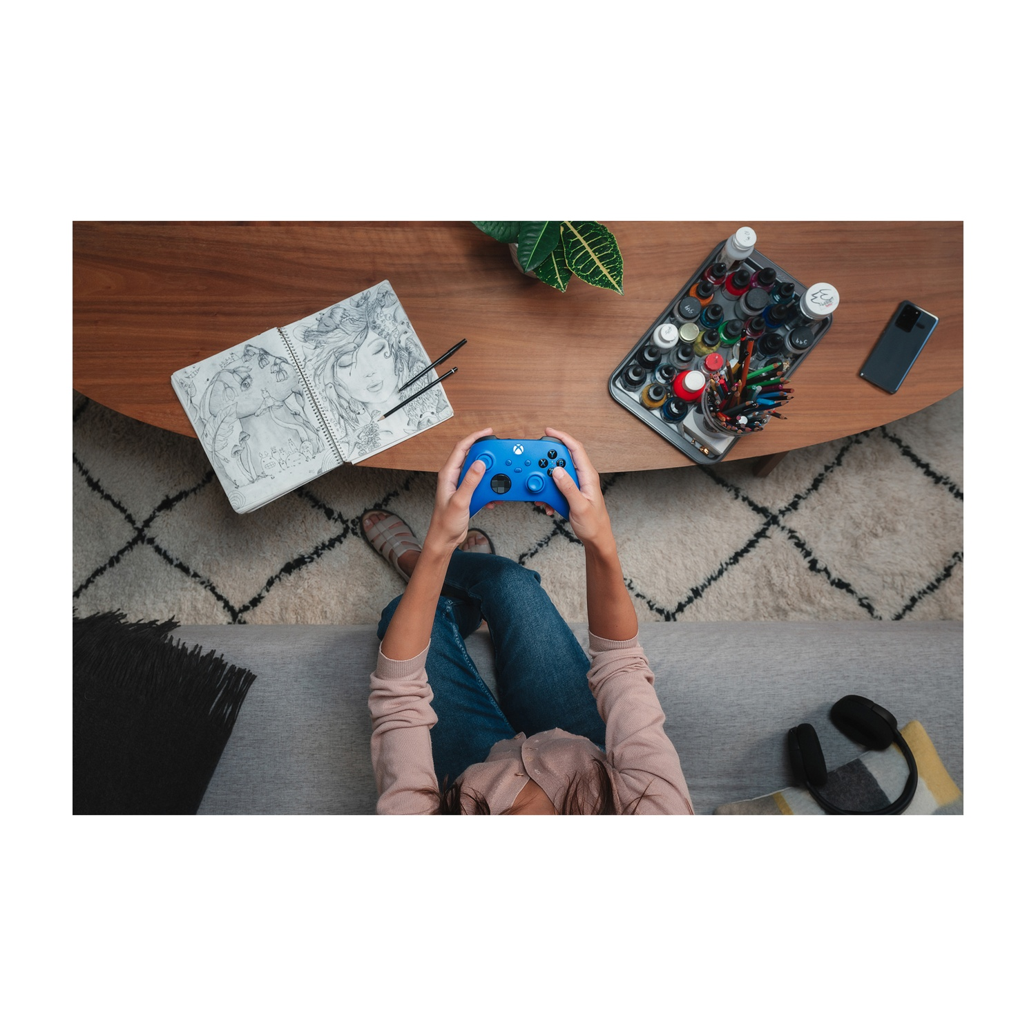 Persoon houdt blauwe controller vast. Tafel met notitieboek, pennen en verf.