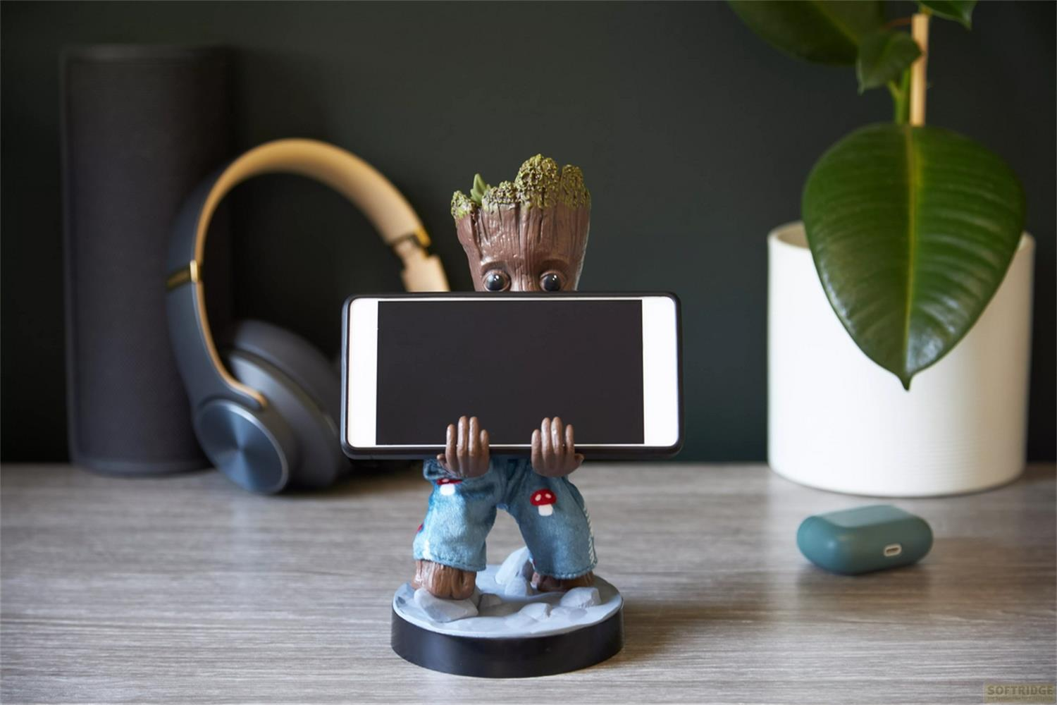 Statua di Groot che tiene uno smartphone; cuffie e pianta vicine.