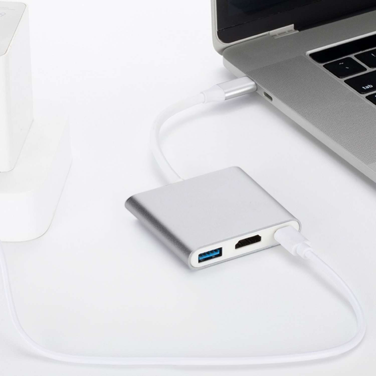Silberner USB-C-Hub mit HDMI- und USB-Anschlüssen, verbunden mit einem Laptop.