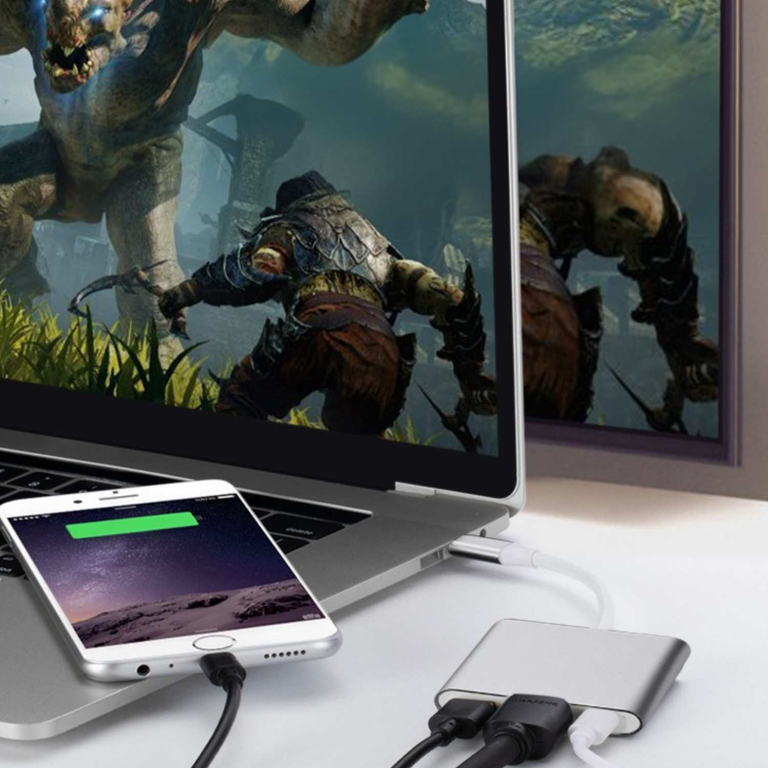 Ein Laptop zeigt ein Videospiel mit einem Monster und Krieger, verbunden mit einem ladenden Telefon und einem Multi-Port-Hub.