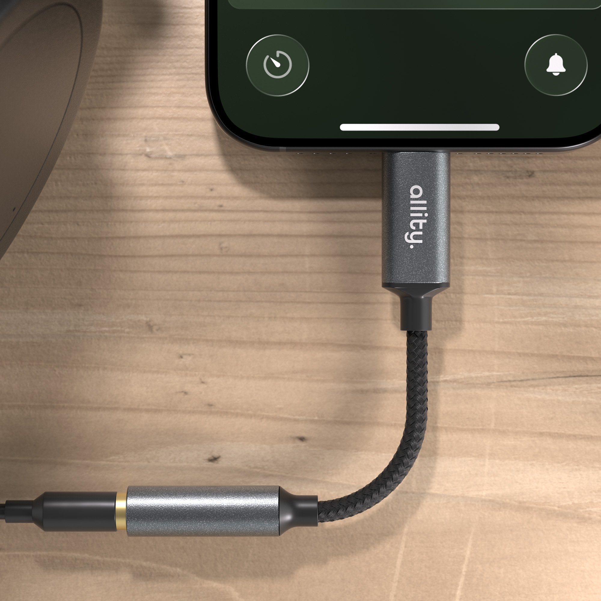 Szary adapter łączy smartfon z głośnikiem na drewnianym tle.