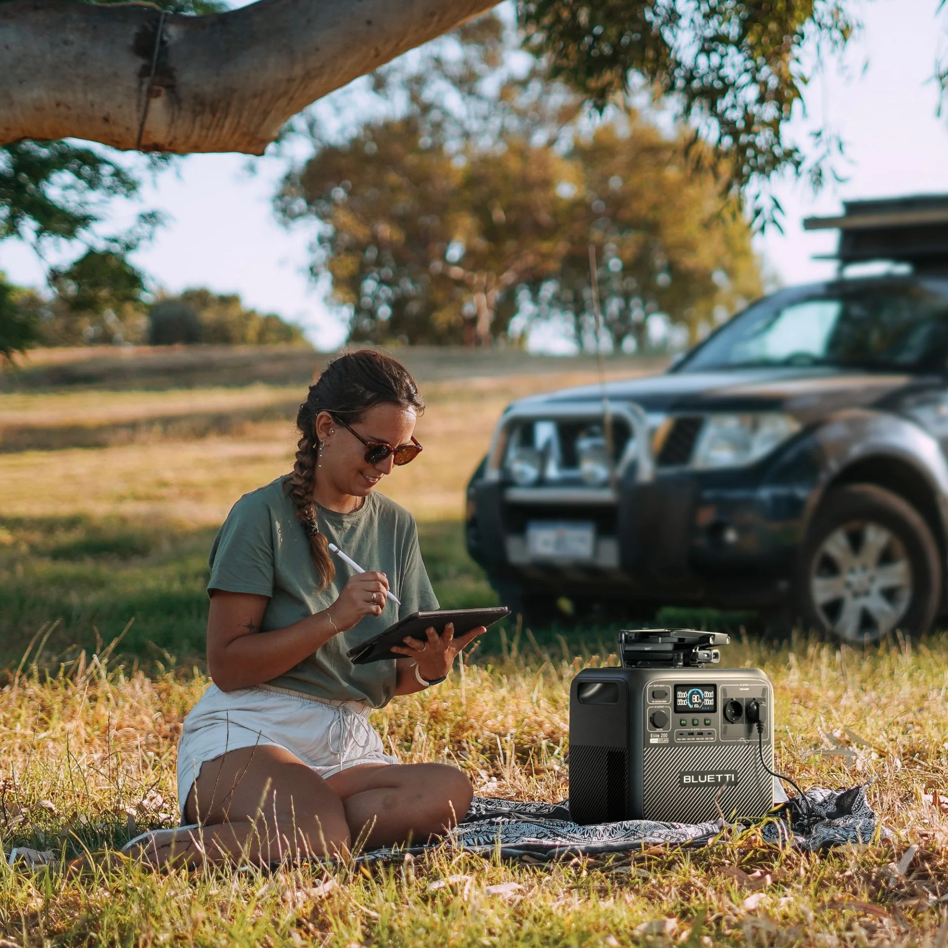 Donna all'aperto usa tablet con power station, auto sullo sfondo.