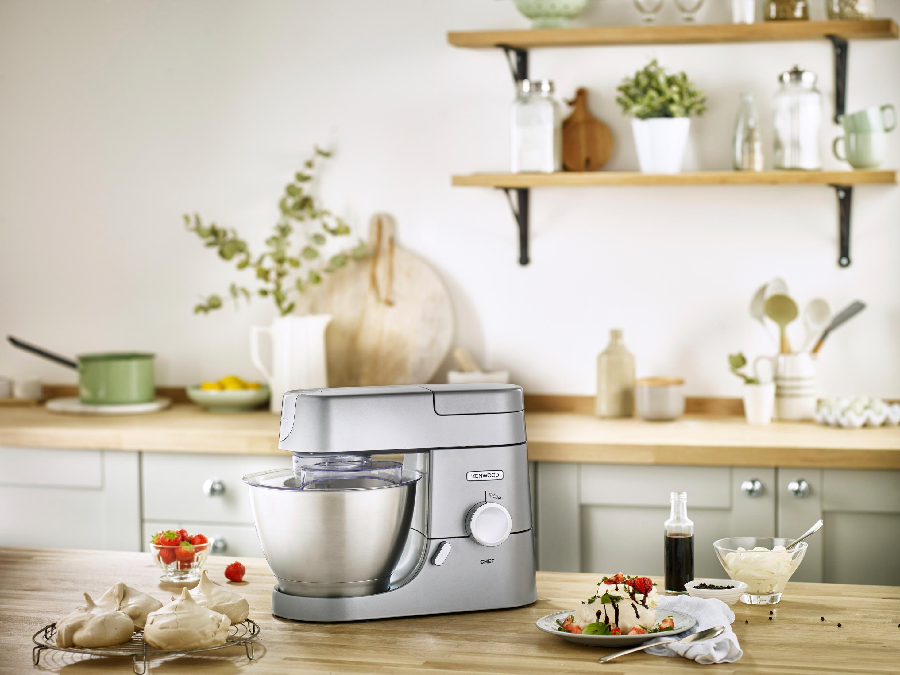 Srebrna robot kuchenny z misą, bezami i truskawkami na drewnianym blacie.