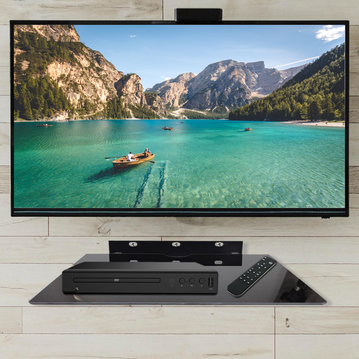 Telewizor płaskoekranowy pokazuje malownicze jezioro z górami. Poniżej odtwarzacz DVD i pilot na półce.