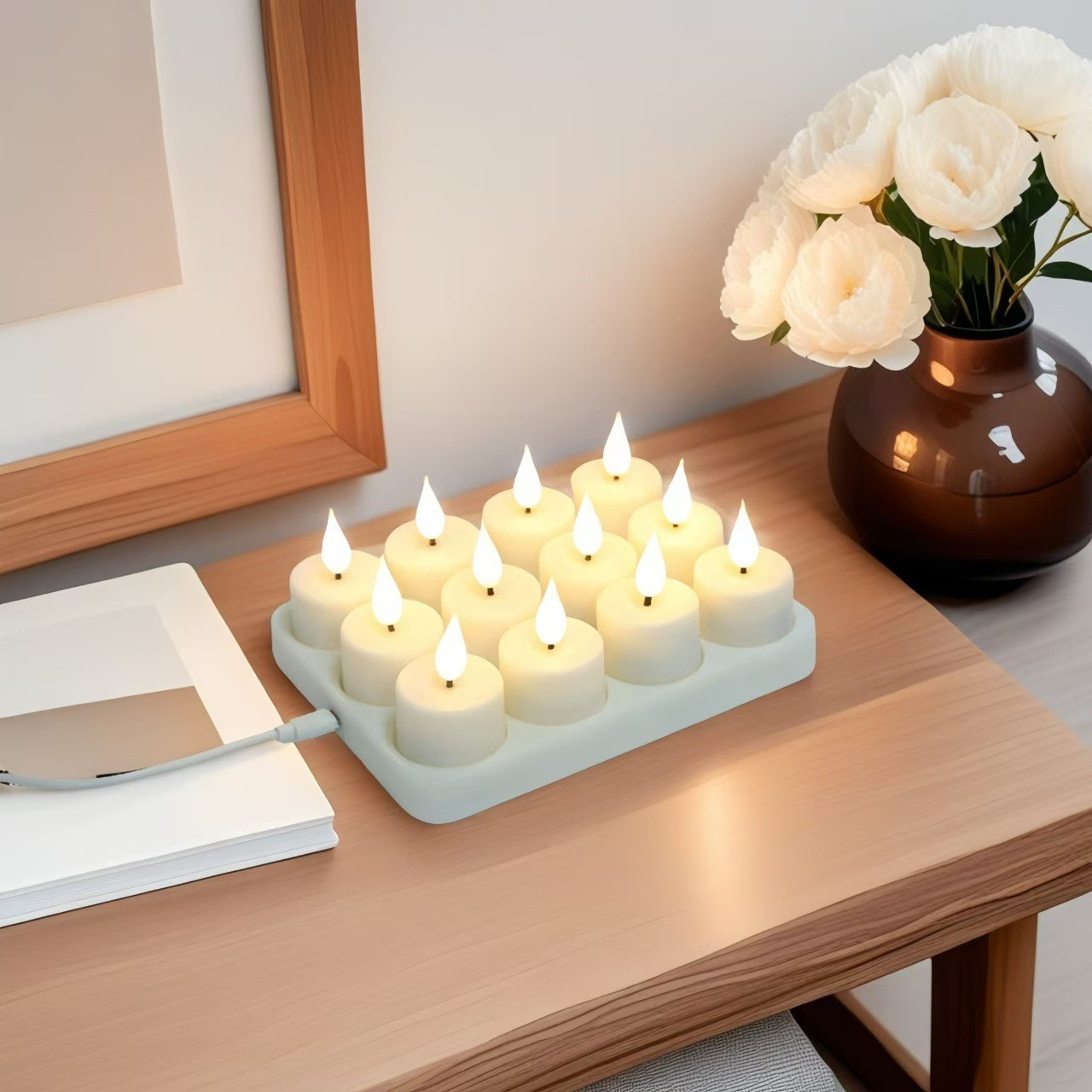 Szesnaście białych podgrzewaczy LED na tacy, obok książki i kwiatów w wazonie.