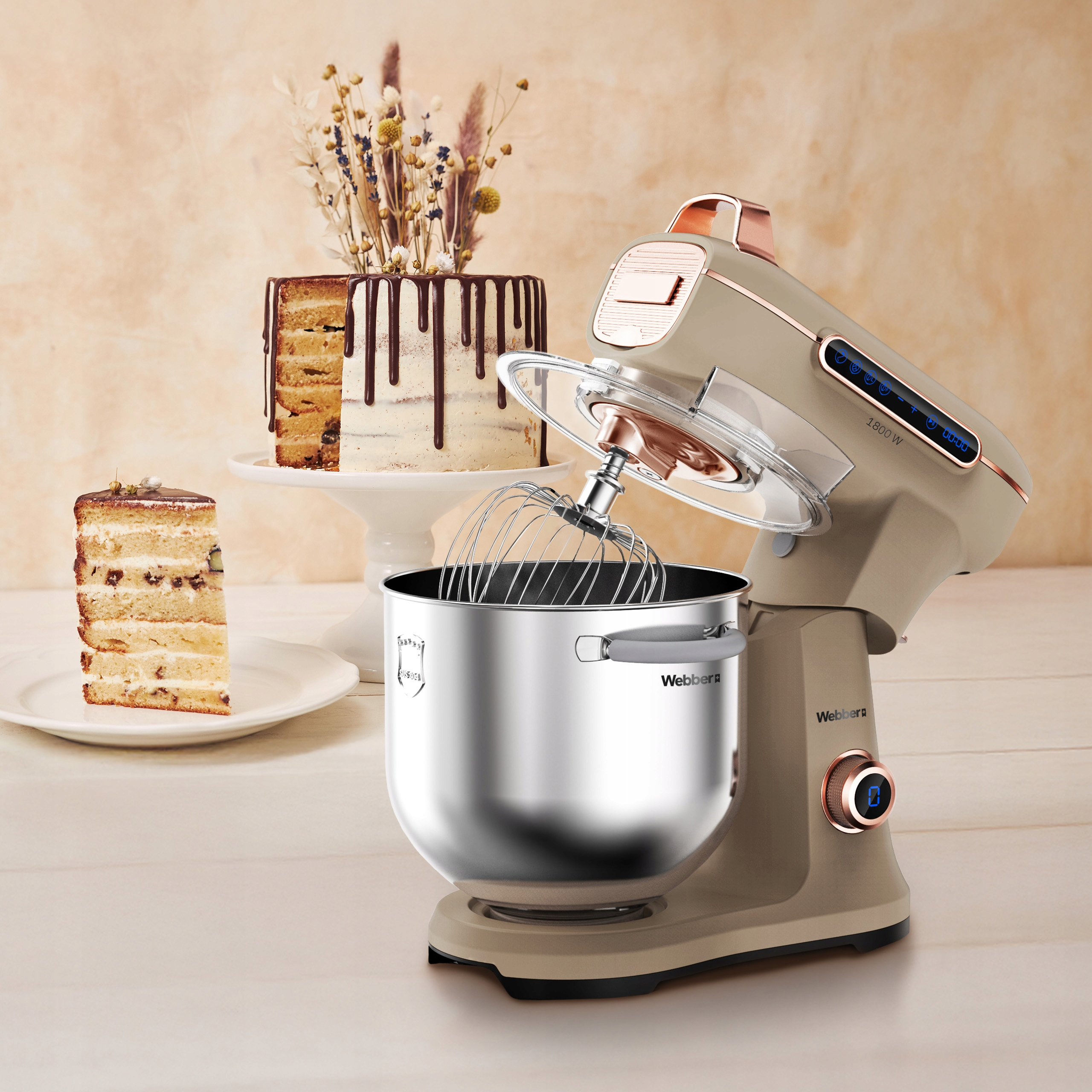 Beżowy mikser stojący obok ciasta na stojaku i kawałka ciasta.