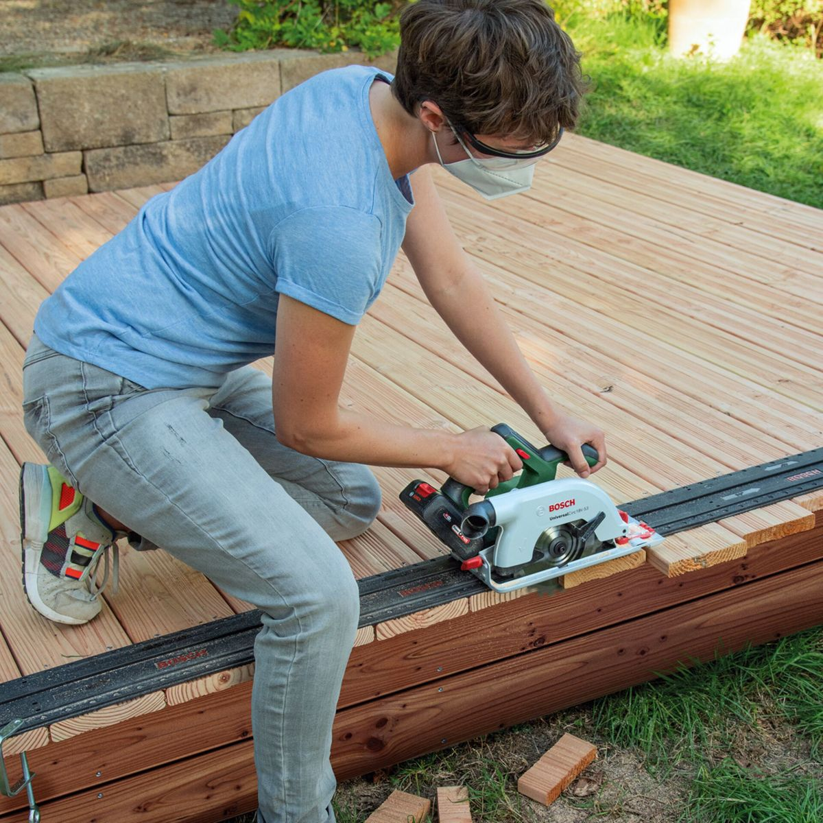 Osoba tnie drewno piłą tarczową na zewnętrznym drewnianym tarasie.