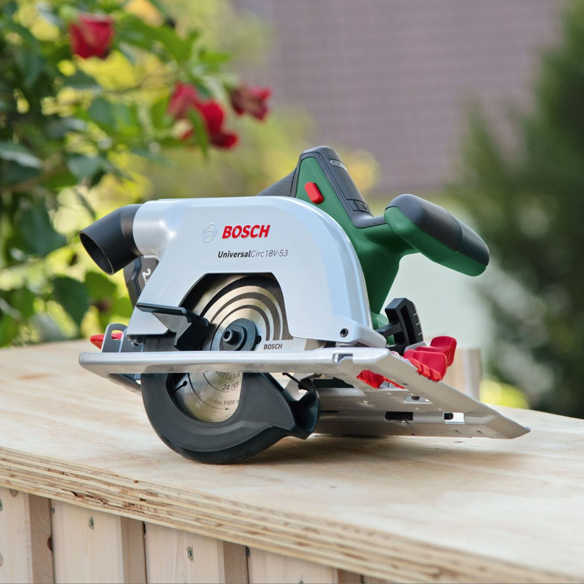 Piła tarczowa Bosch spoczywa na drewnianych deskach z czerwonymi kwiatami w tle.