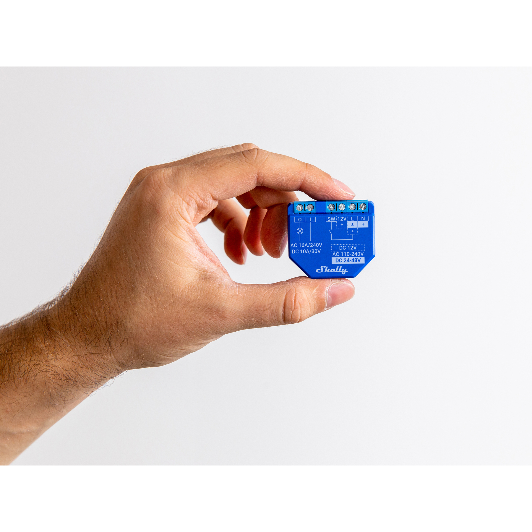 Una mano sostiene un pequeño dispositivo Shelly azul con conectores.