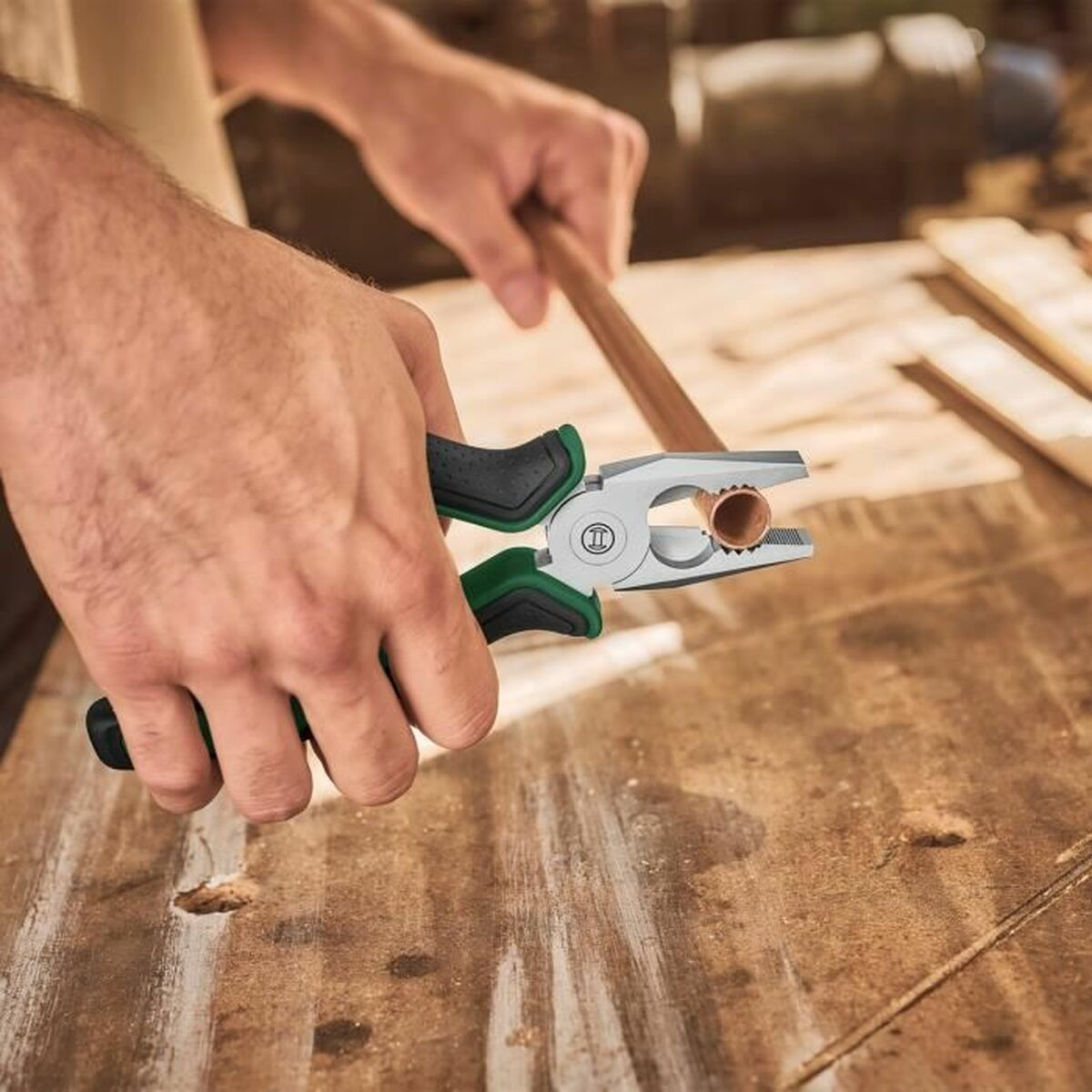 Hände halten Zange mit Kupferrohr auf Holztisch.