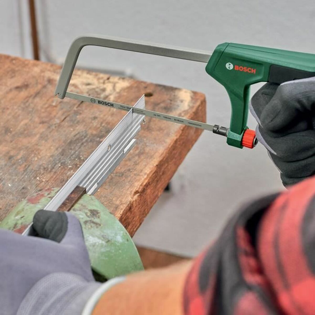 Person sägt Metallprofil mit Bosch Säge auf Holzbalken.