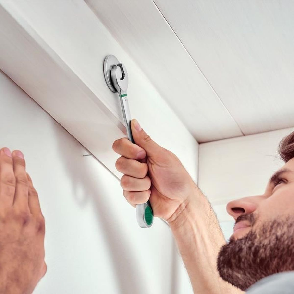 Mann benutzt Ratschenschlüssel, um eine weiße Halterung an einer weißen Wand zu befestigen.