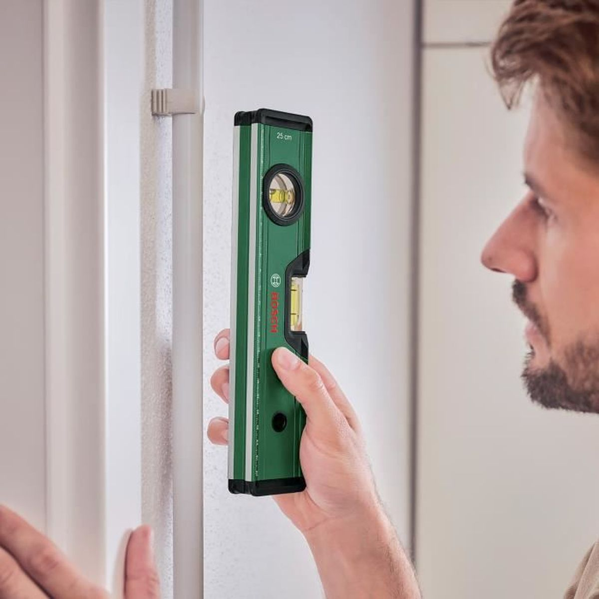 Mann hält grüne Wasserwaage an eine Wand mit einer Leiste.