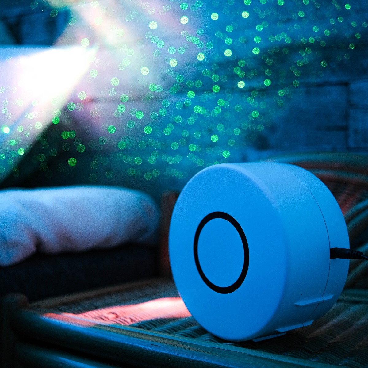 Ein blauer Projektor wirft grüne Lichtpunkte auf eine Holzwand und ein Bett.
