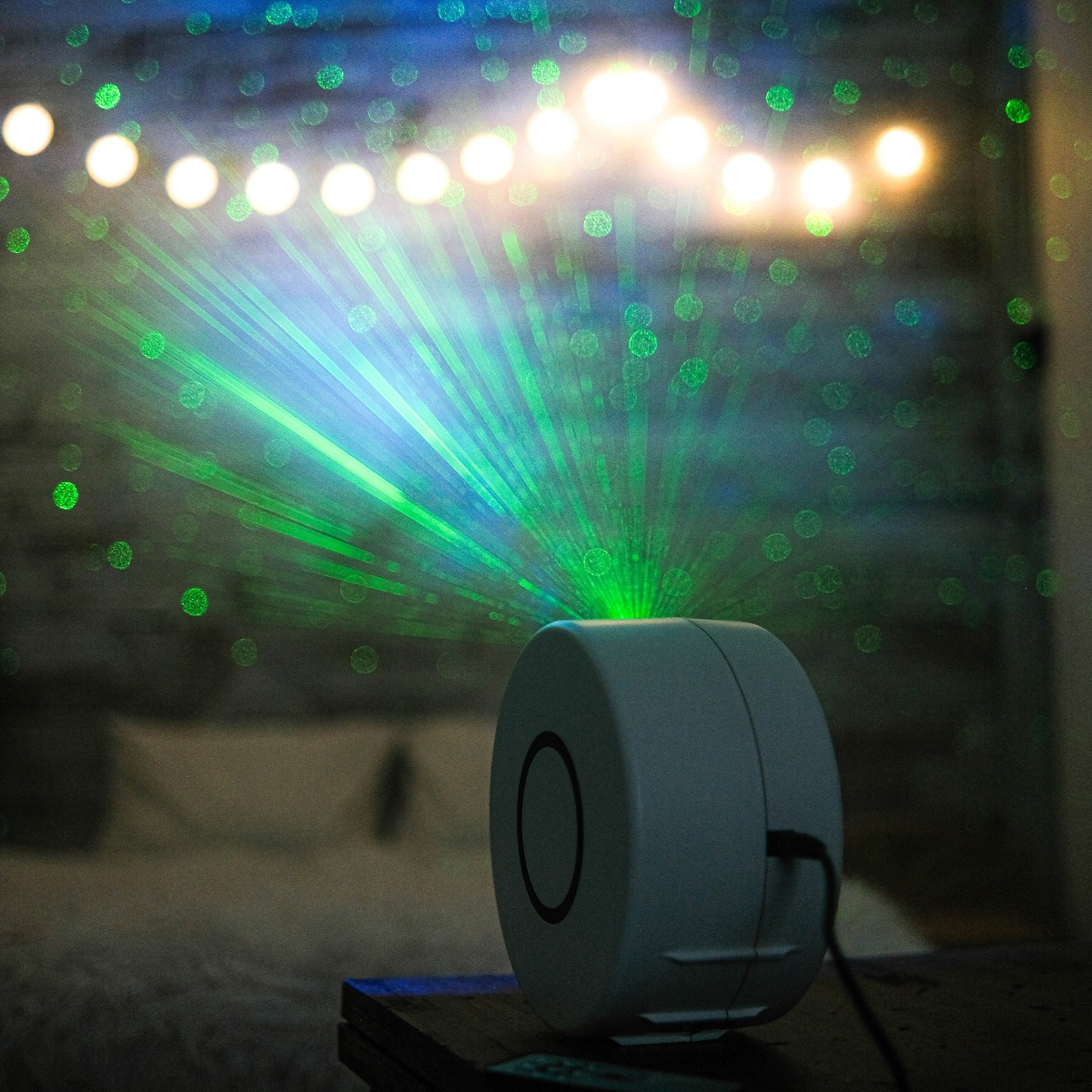 Ein weißer Projektor sendet grüne Laserstrahlen in einen dunklen Raum mit Lichtern.