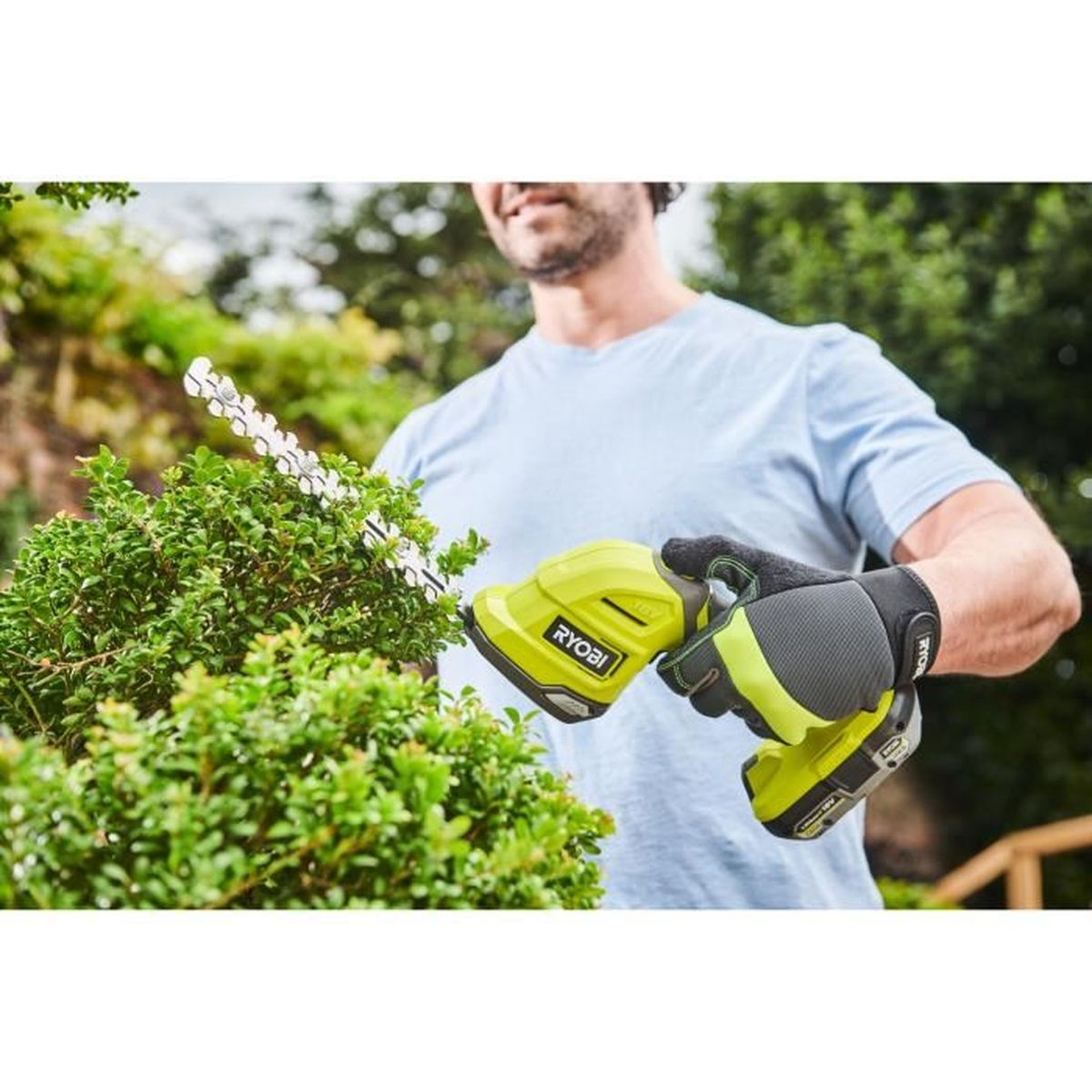 Mann trimmt grüne Büsche mit einem gelben Ryobi-Hochentaster im Garten.
