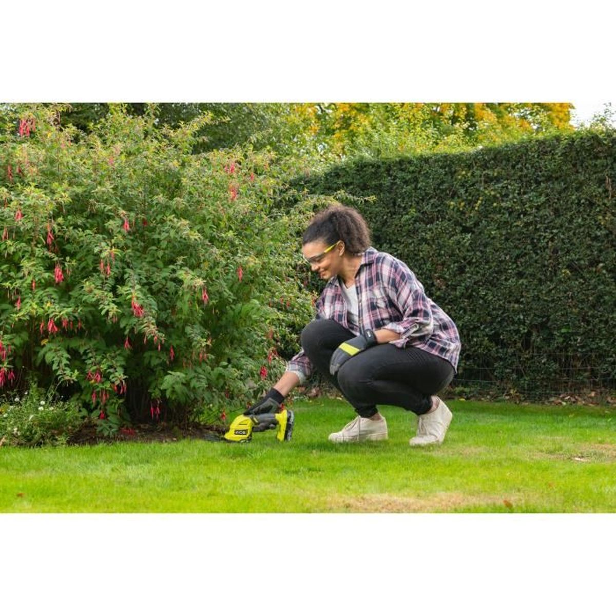 Frau trimmt Busch mit Heckenschere im Garten.