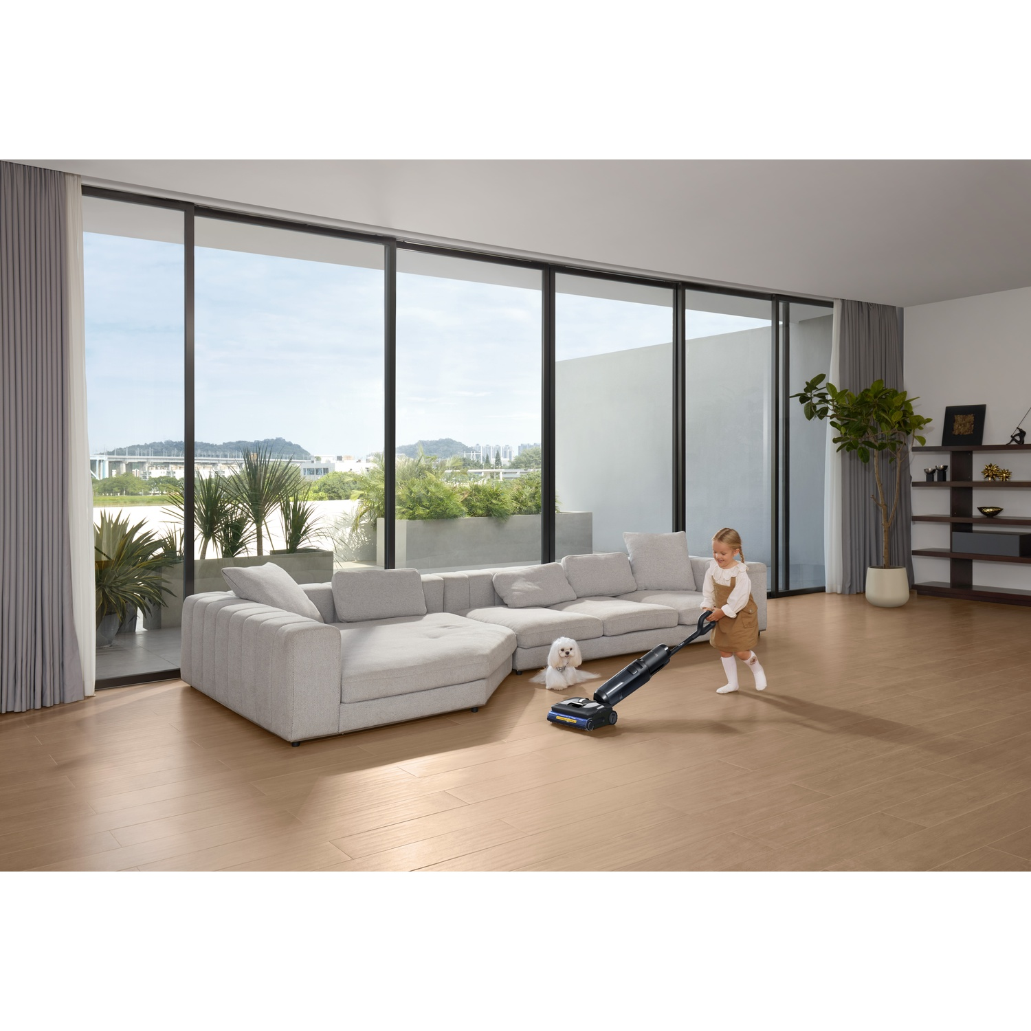 Mała dziewczynka odkurza niebieskim odkurzaczem, pies obserwuje.