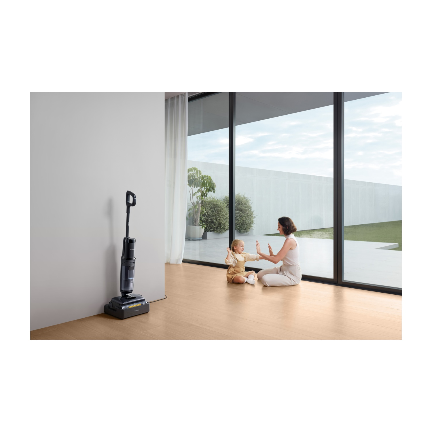 Kobieta i dziecko bawią się na podłodze, obok stoi odkurzacz.