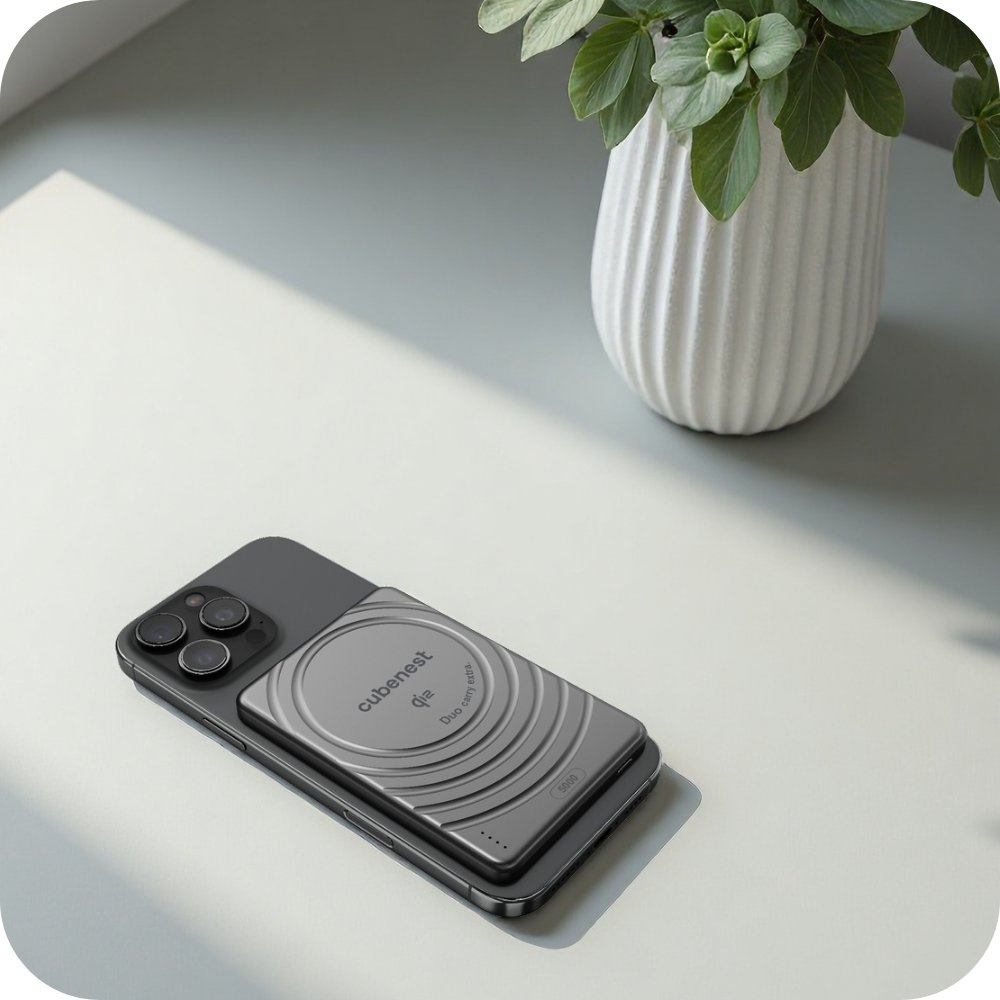 Ein graues Handy mit einer magnetischen Powerbank liegt auf einem Tisch. Eine Vase mit Pflanzen steht im Hintergrund.