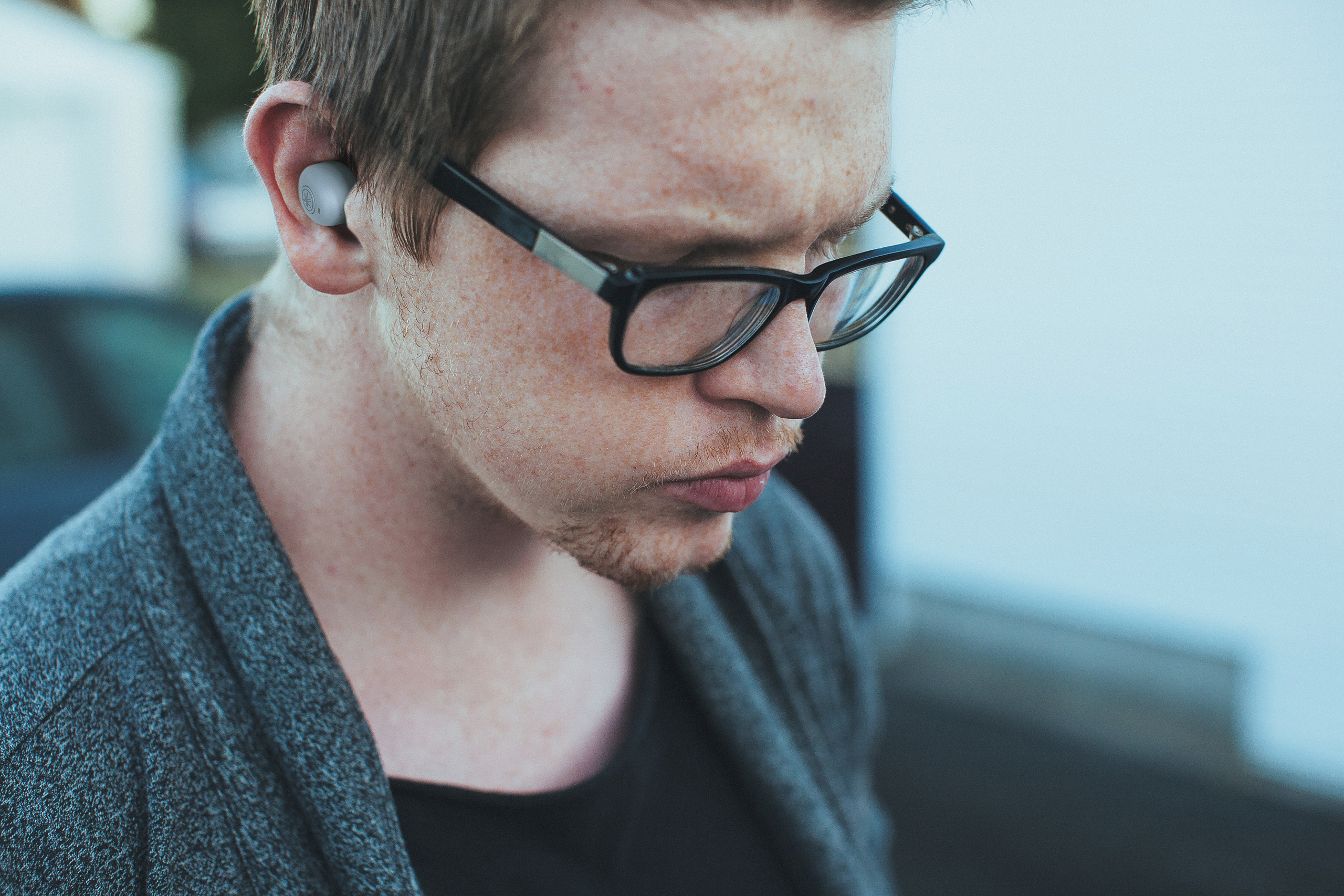 Nahaufnahme eines Mannes mit Brille und grauem Ohrhörer.