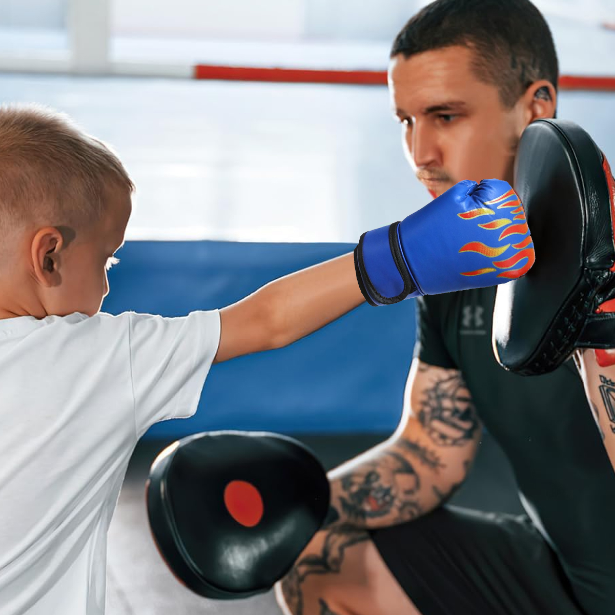 Ein Kind mit blauen Boxhandschuhen boxt gegen ein Schlagpolster, das ein Trainer hält.