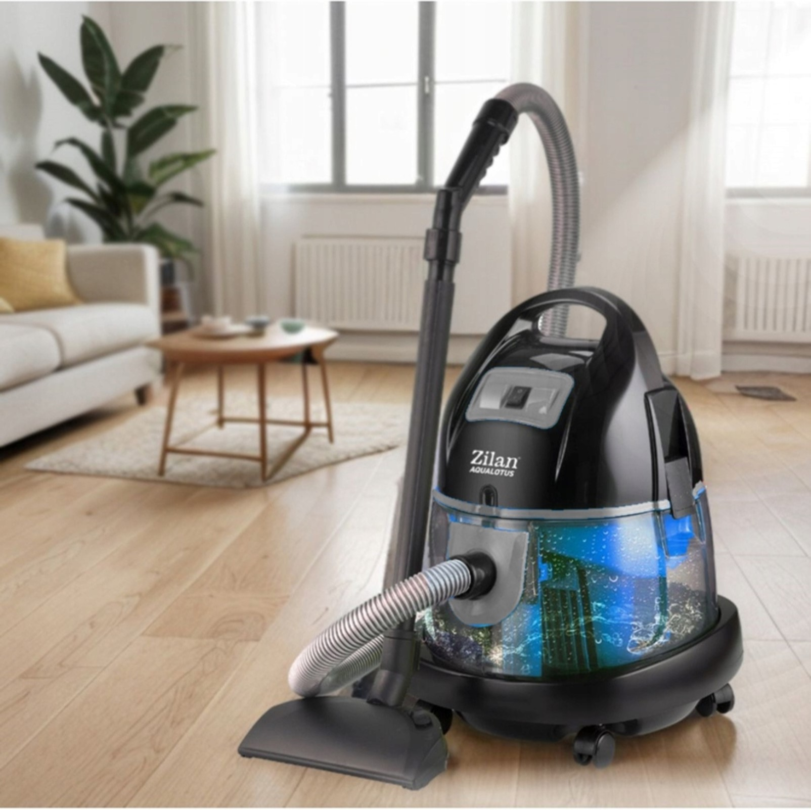 Czarny odkurzacz Zilan Aqualotus z przezroczystym zbiornikiem na wodę, pokazującym niebieską wodę i bąbelki, w salonie.
