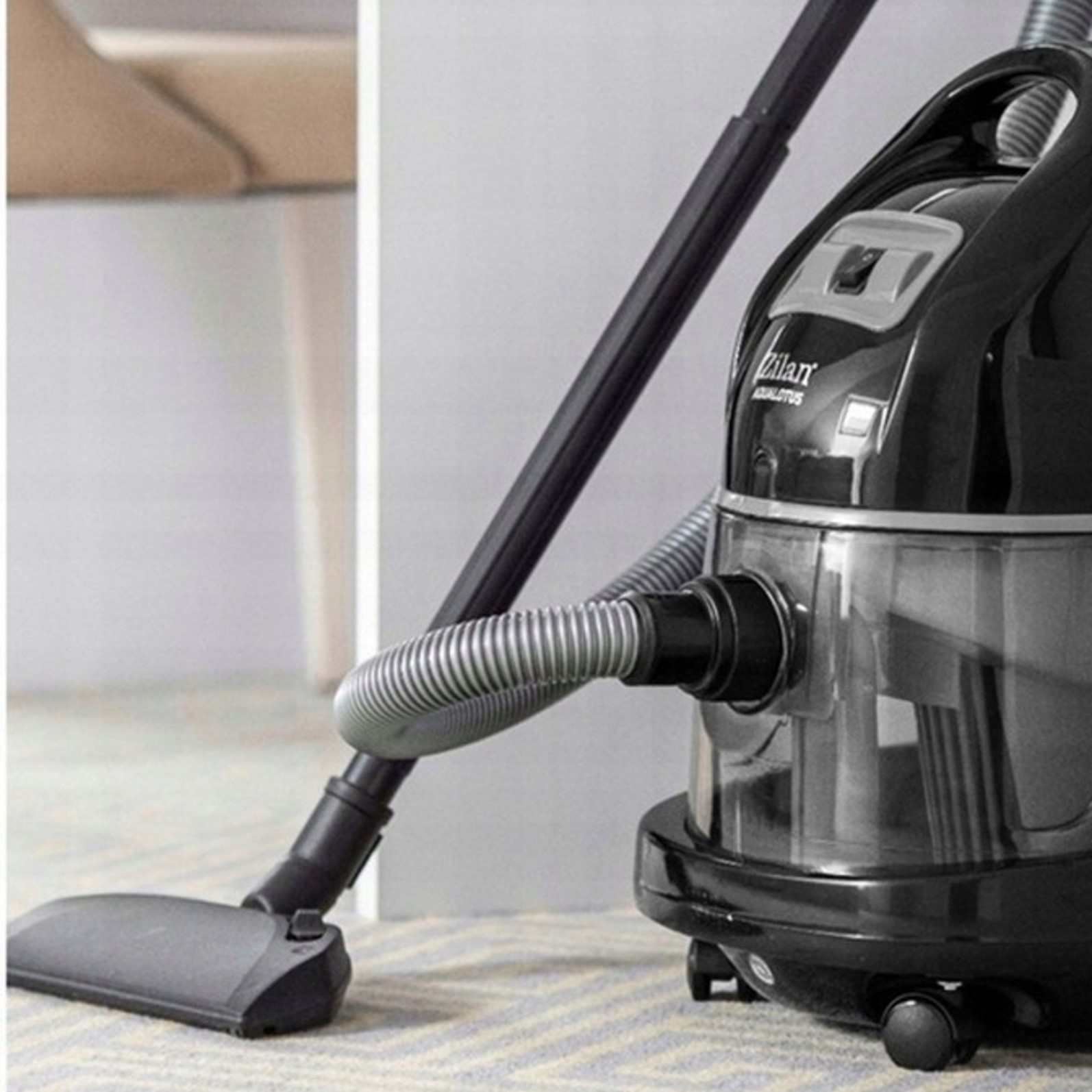 Czarny odkurzacz z wężem i szczotką na dywanie.