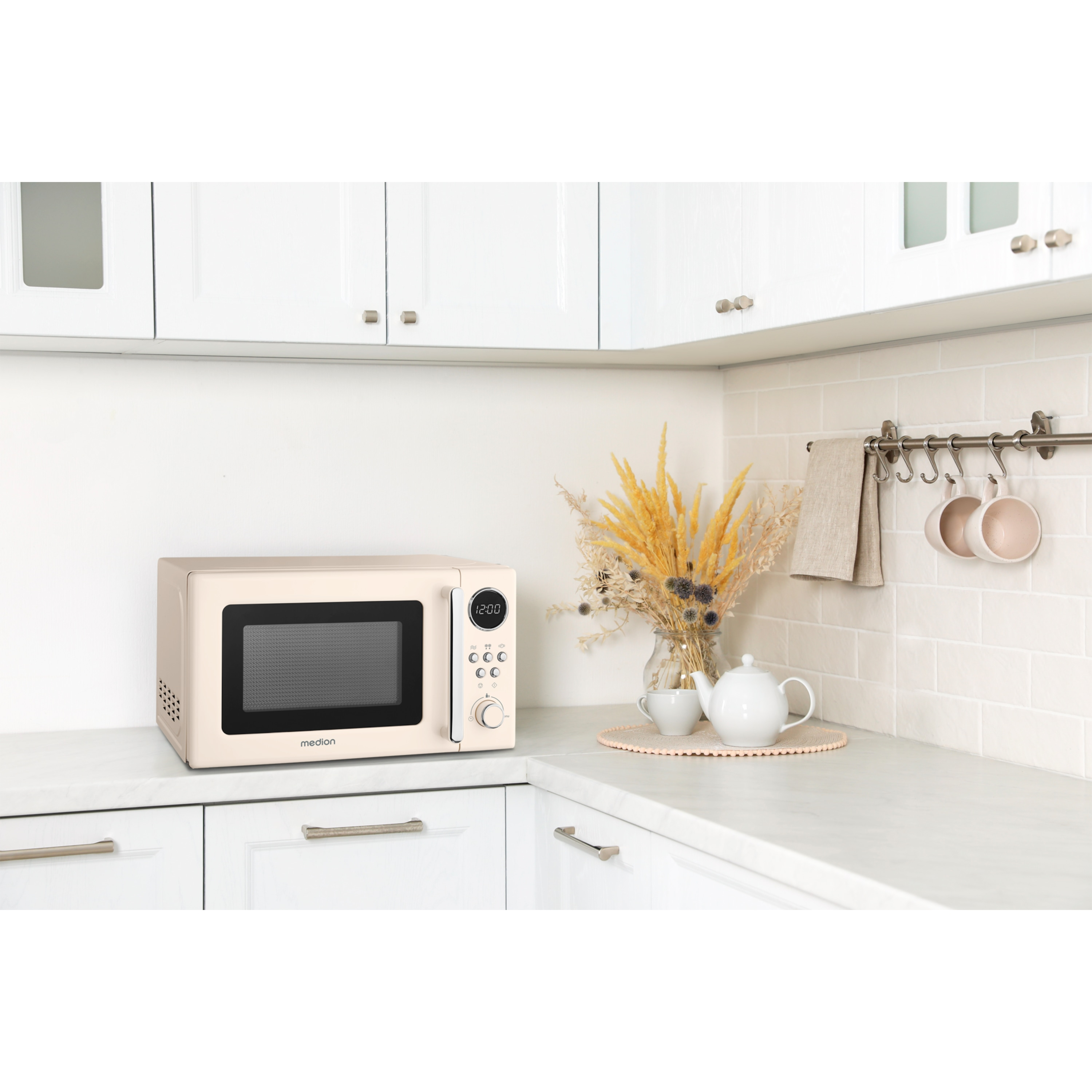 Kremowa kuchenka mikrofalowa stoi na blacie obok wazonu z suszonymi kwiatami.