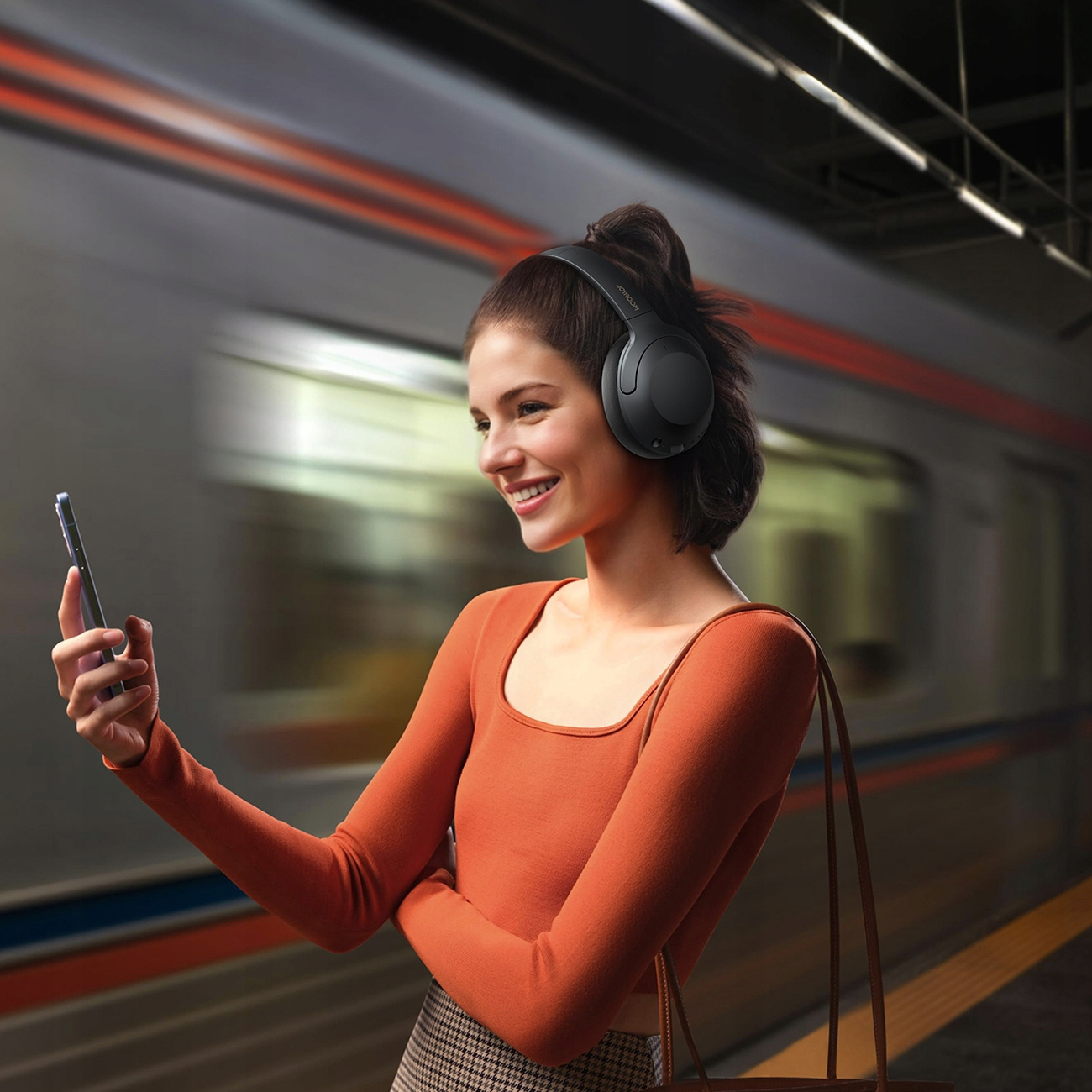 Kobieta w słuchawkach trzyma smartfona, gdy obok przejeżdża pociąg.