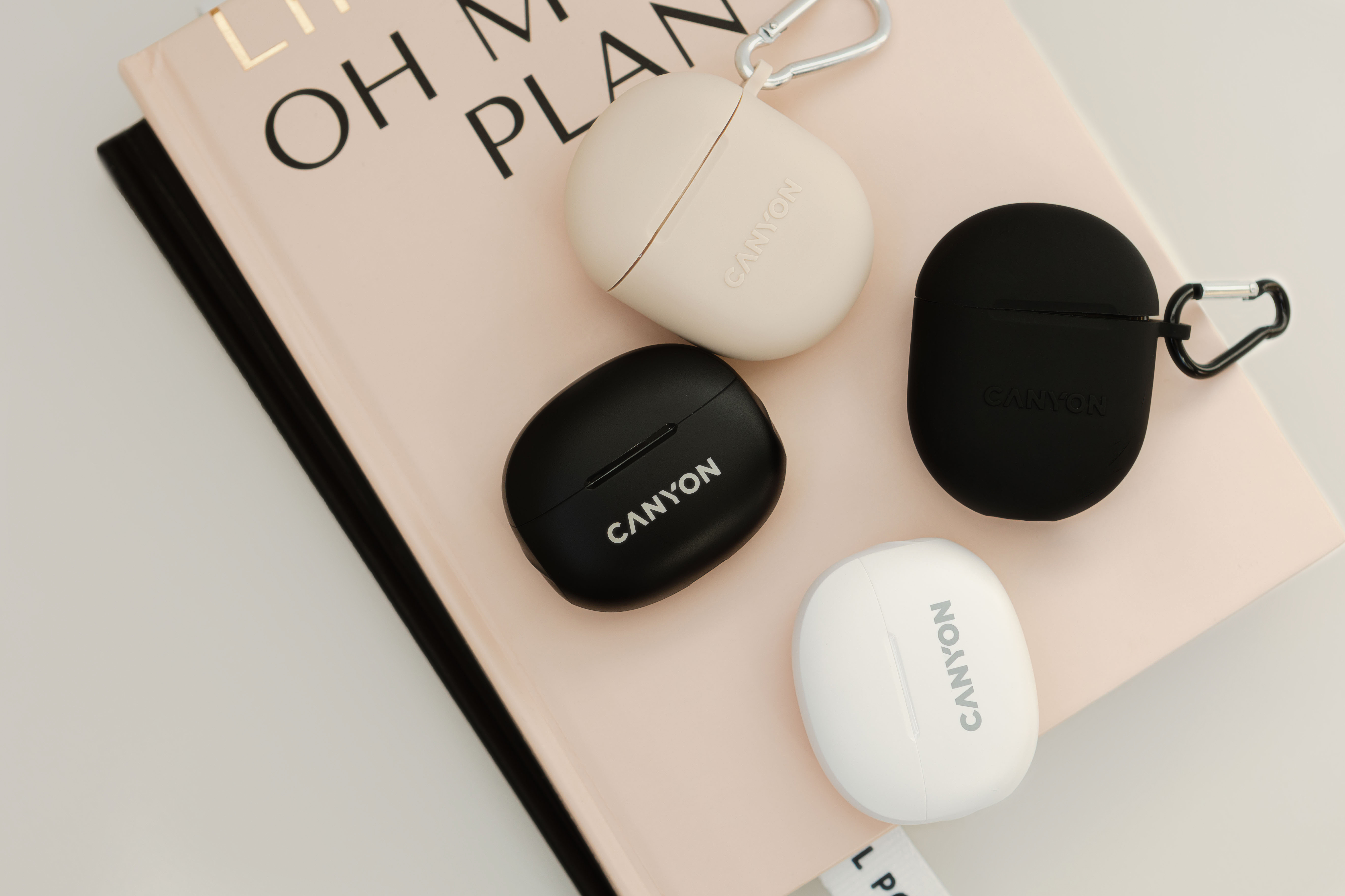 Cztery etui na słuchawki Canyon w kolorach czarnym, białym i beżowym leżą na książce.