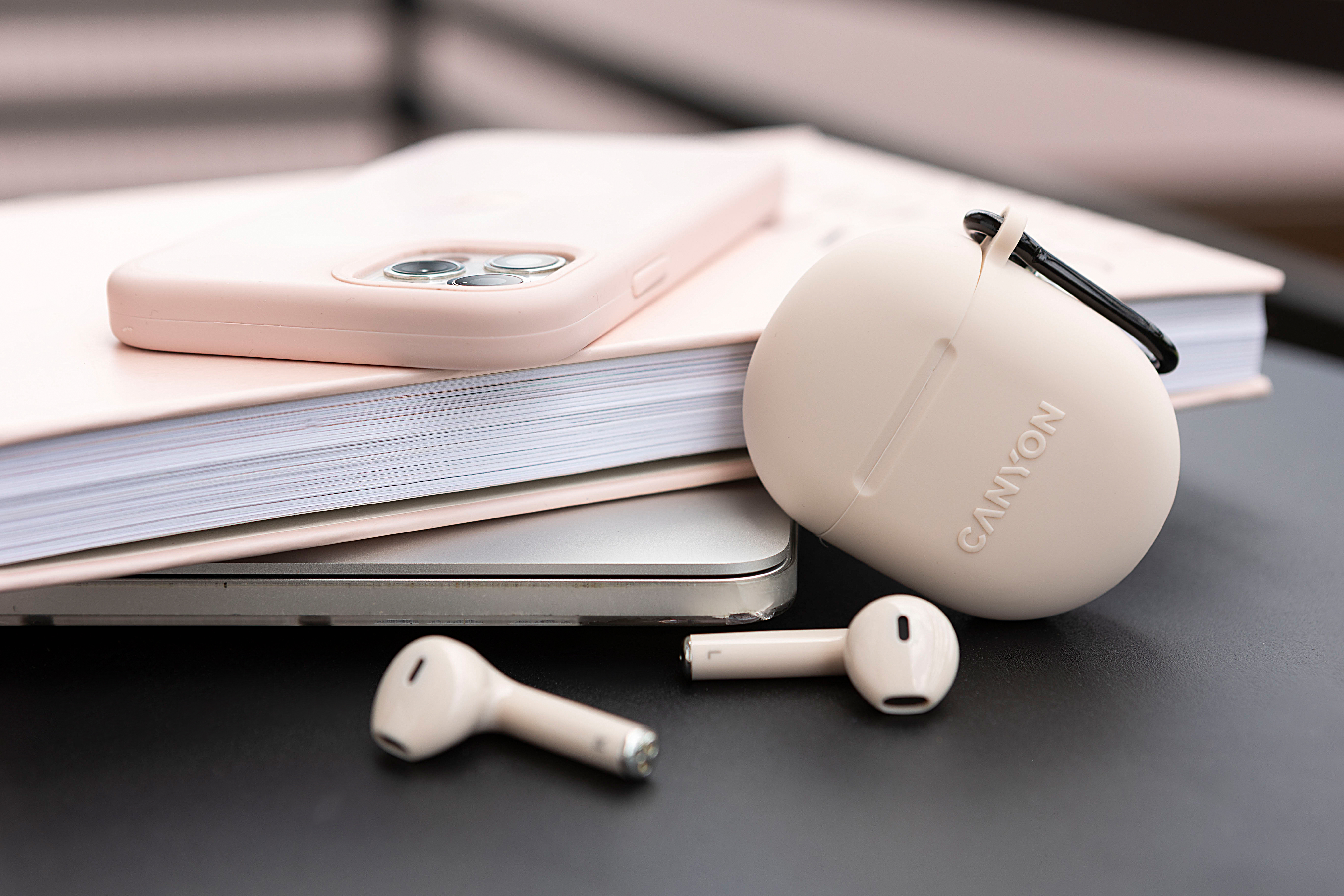 Różowy iPhone, notatnik, laptop i słuchawki na biurku.