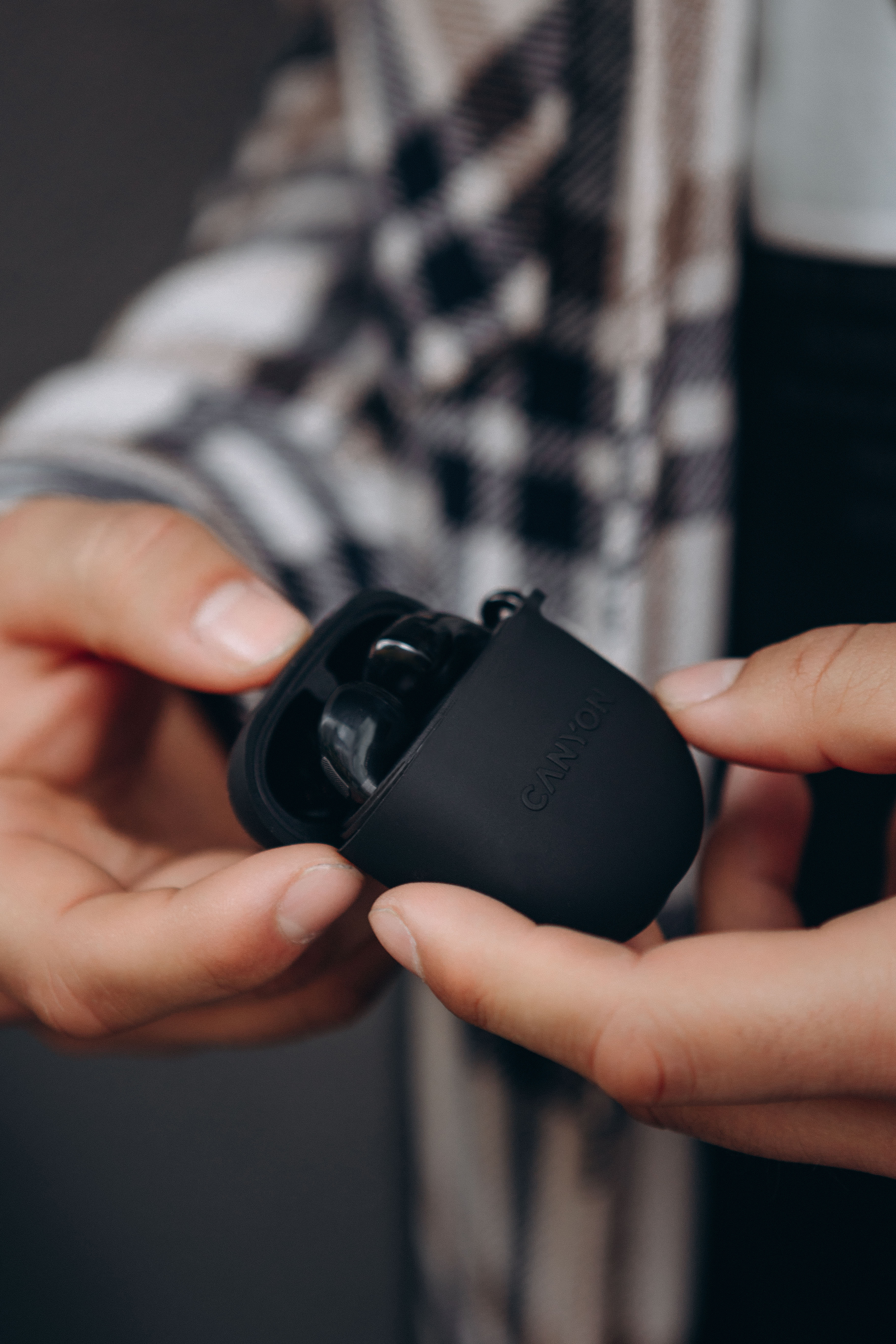 Dłonie trzymające czarne etui ładujące z logo Canyon i słuchawkami.