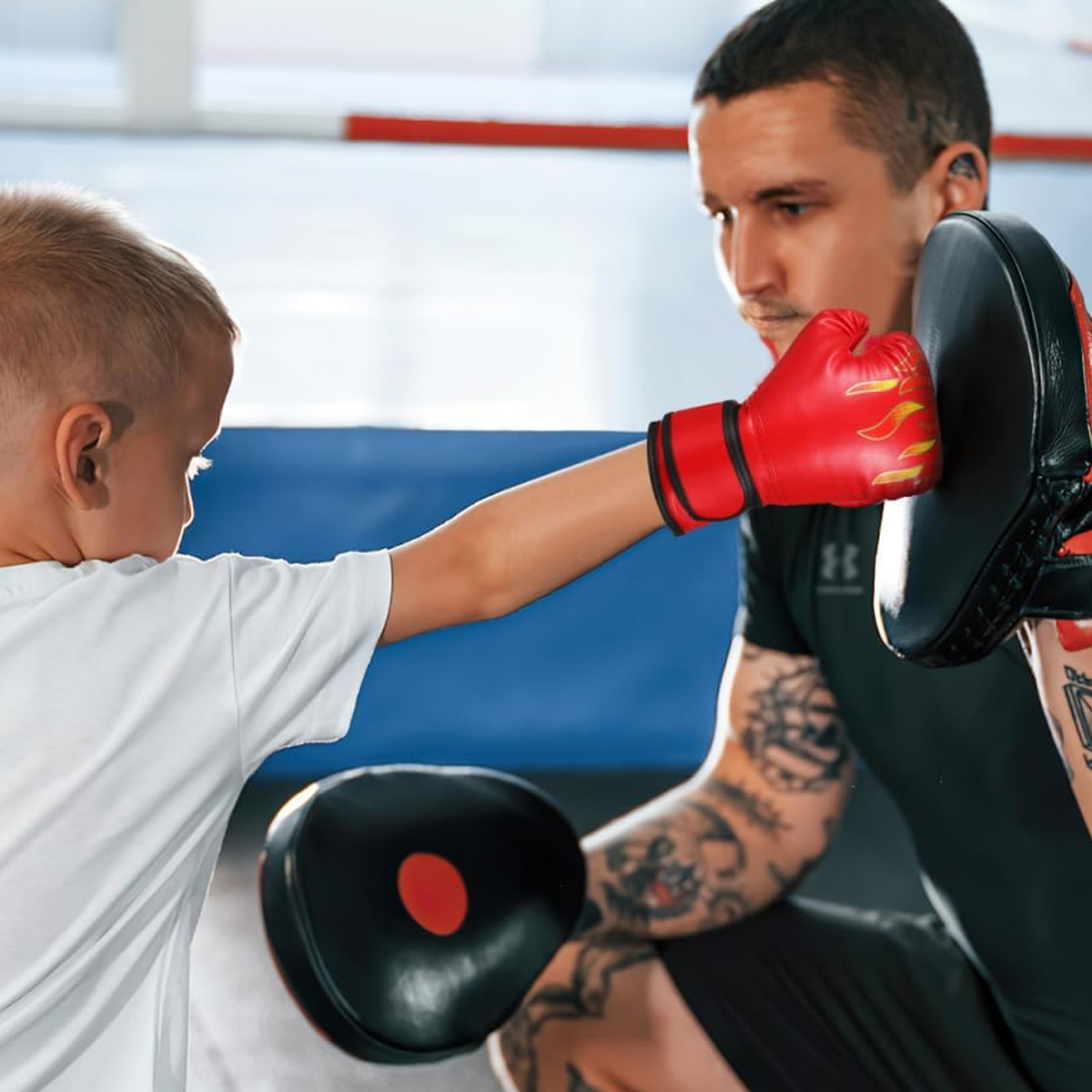 Ein Junge mit roten Boxhandschuhen schlägt auf ein Polster, das ein Trainer hält.