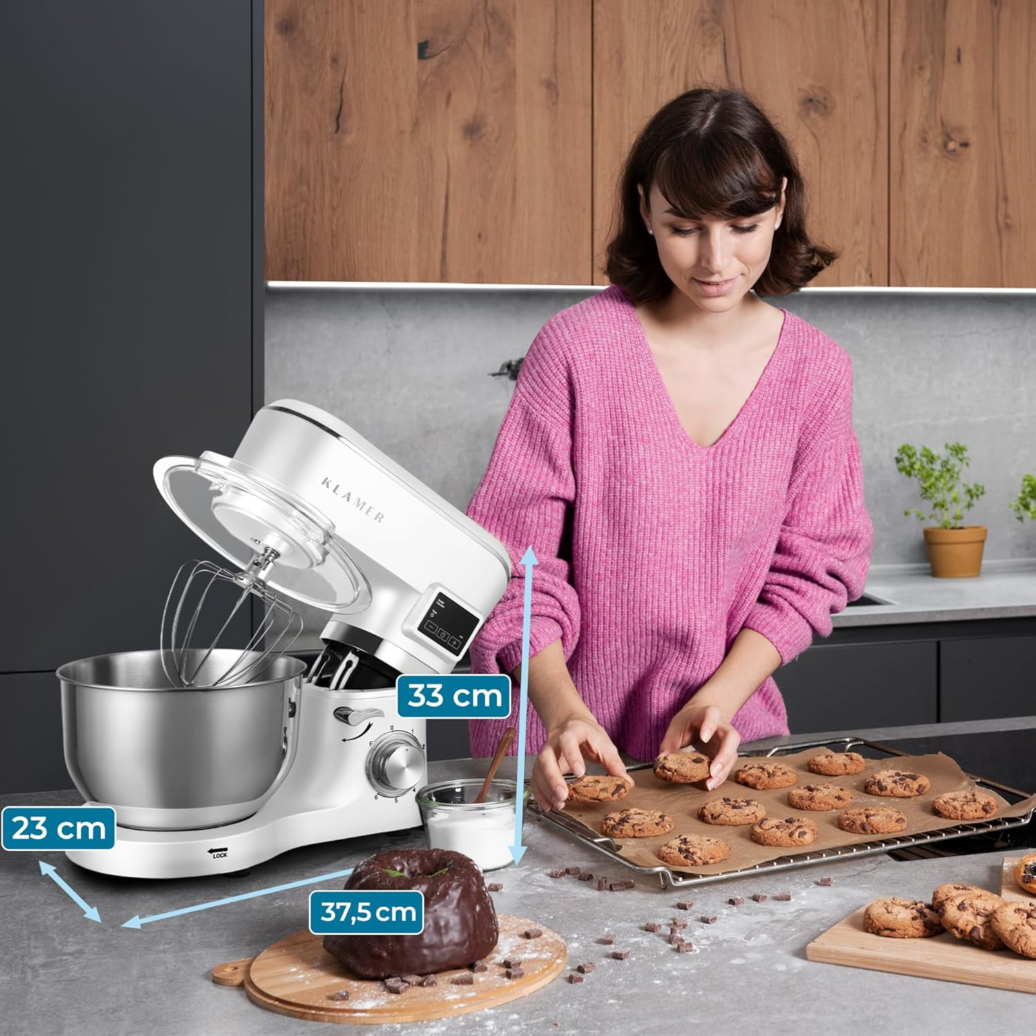 Eine Frau mit einem pinken Pullover arrangiert Kekse auf einem Backblech neben einem Küchenmixer.