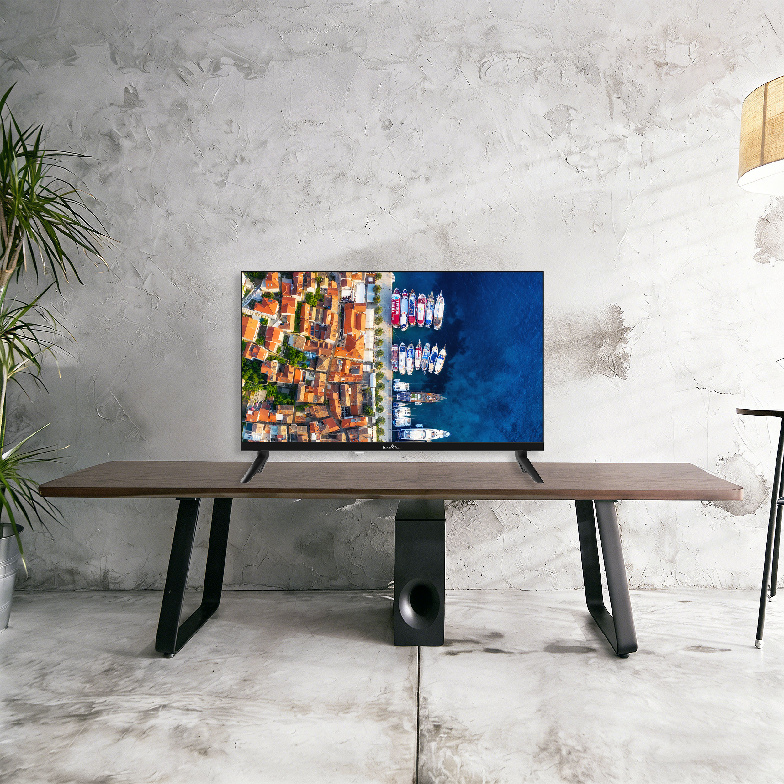 Un televisor moderno sobre una mesa de madera, mostrando una vista aérea de un pueblo costero con barcos.