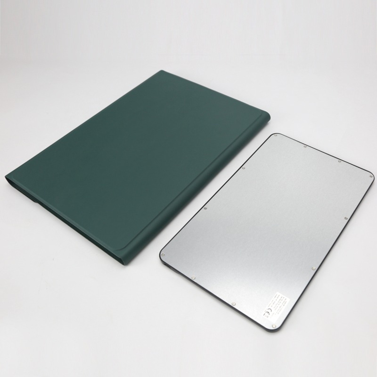 Una custodia verde scuro giace accanto a un tablet argentato su sfondo bianco.