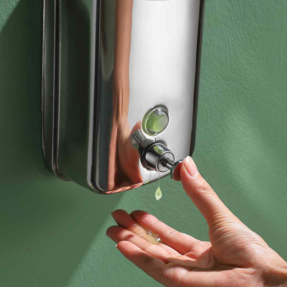 Hand drückt Seifenspender, Flüssigkeit tropft in Handfläche. Grüne Wand.