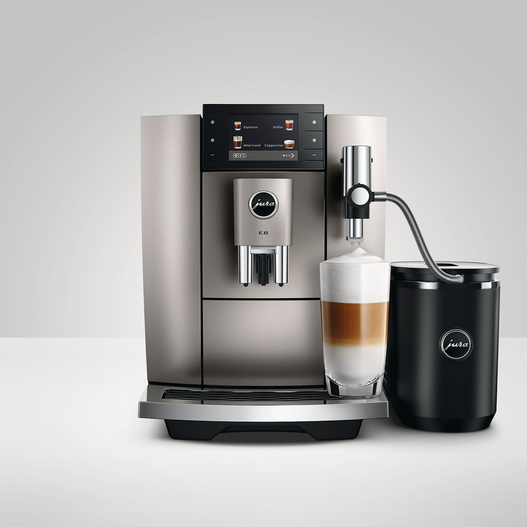 Macchina da caffè Jura argentata con bicchiere di latte macchiato e contenitore latte nero.