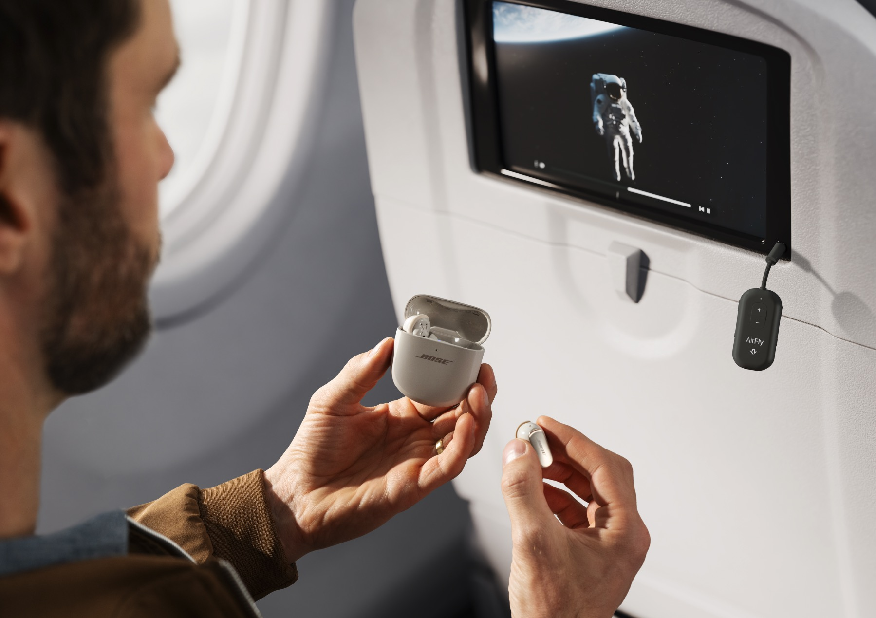 Uomo in aereo tiene auricolari e custodia davanti a schermo con astronauta.