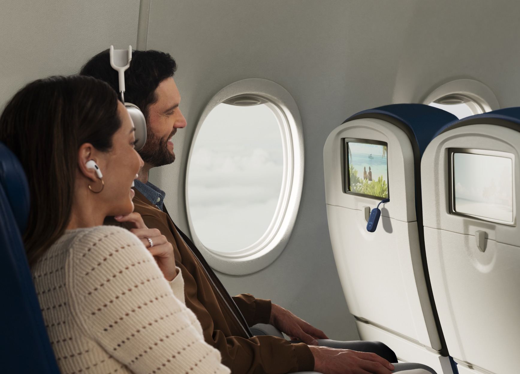 Coppia in aereo con cuffie, guarda schermo e finestra.