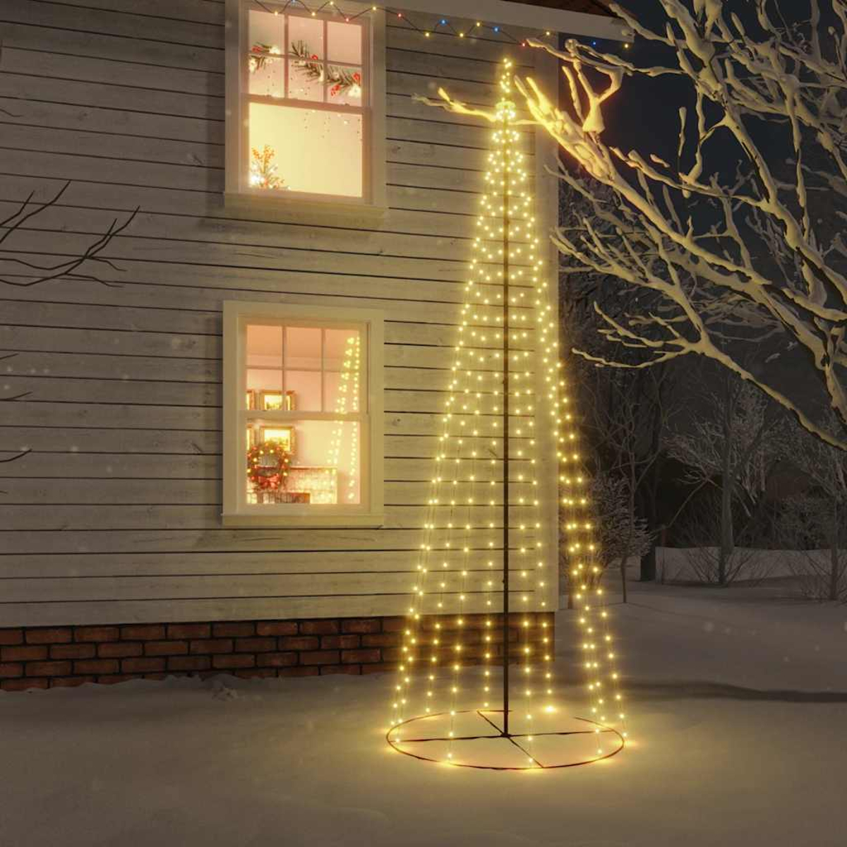 Ein beleuchteter Tannenbaum aus Lichtern steht im Schnee vor einem Haus mit Fenstern.