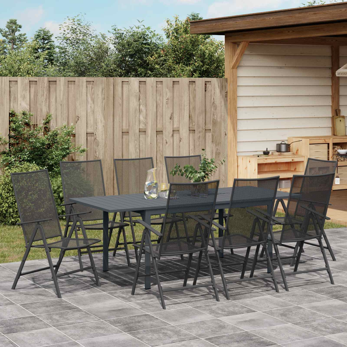 Gartensitzgruppe mit grauem Tisch und Stühlen auf gefliester Terrasse am Holzzaun.