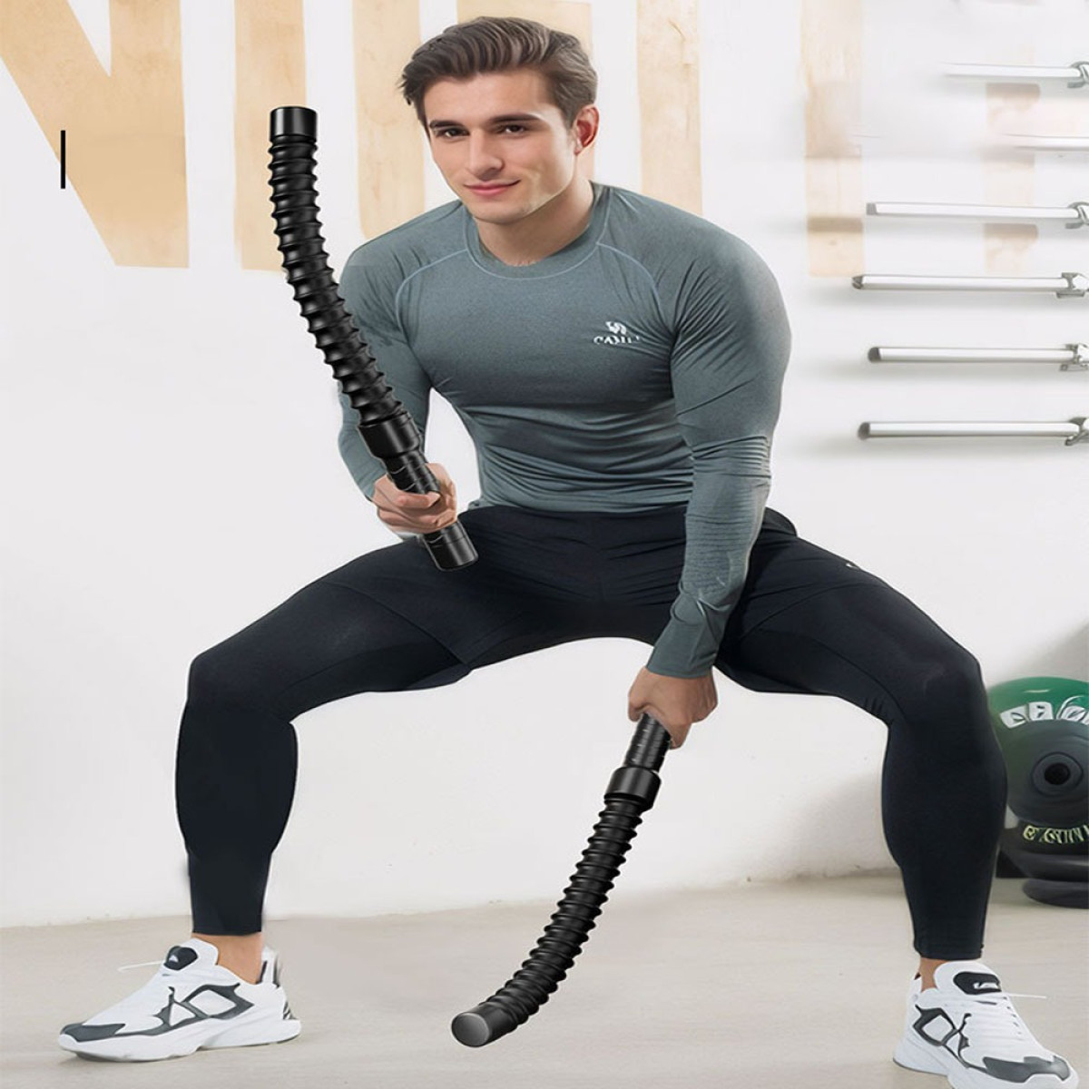 Mężczyzna w stroju sportowym trzyma dwie czarne, elastyczne drążki w siłowni.