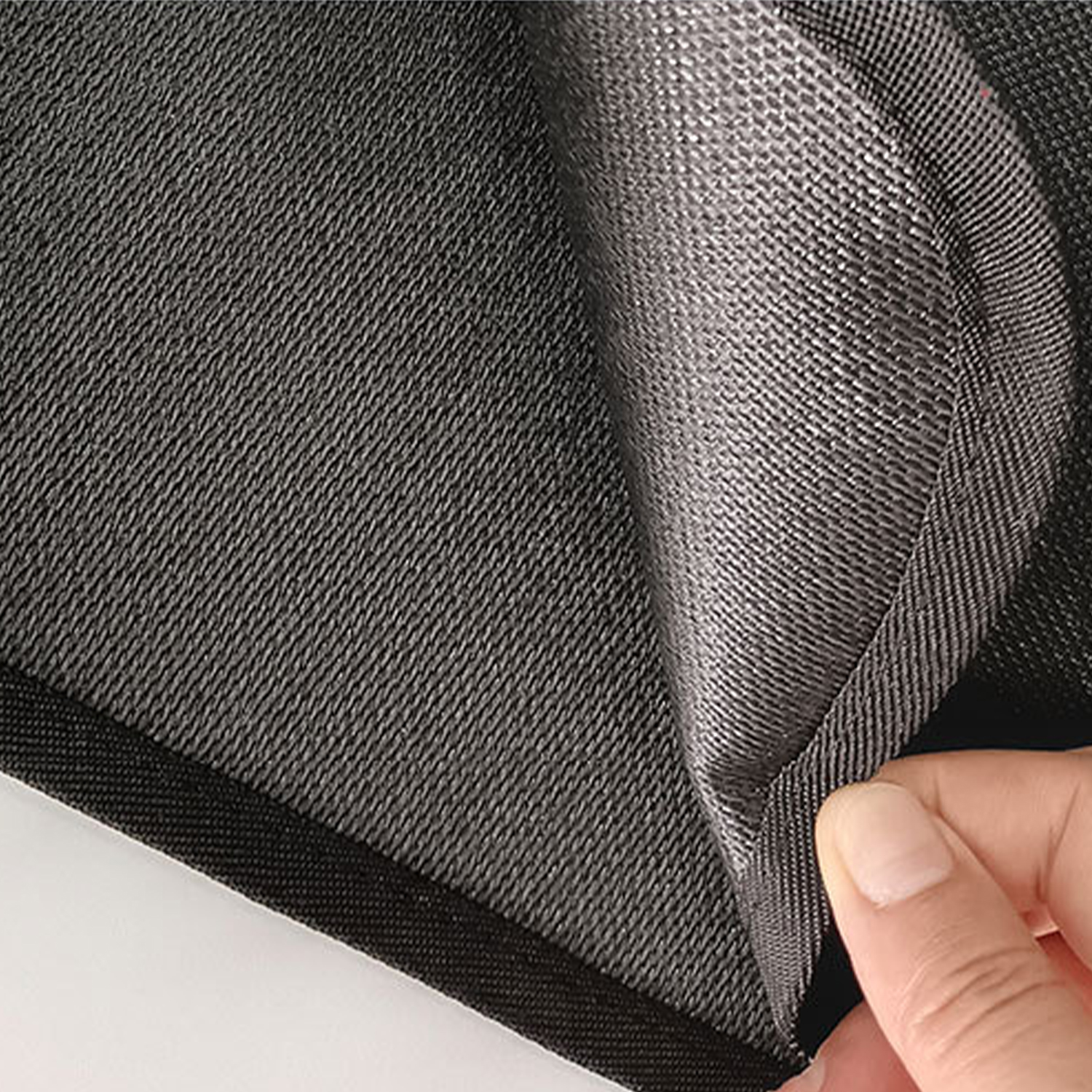 Ręka podnosi szarą tkaninę, odsłaniając błyszczącą powierzchnię.