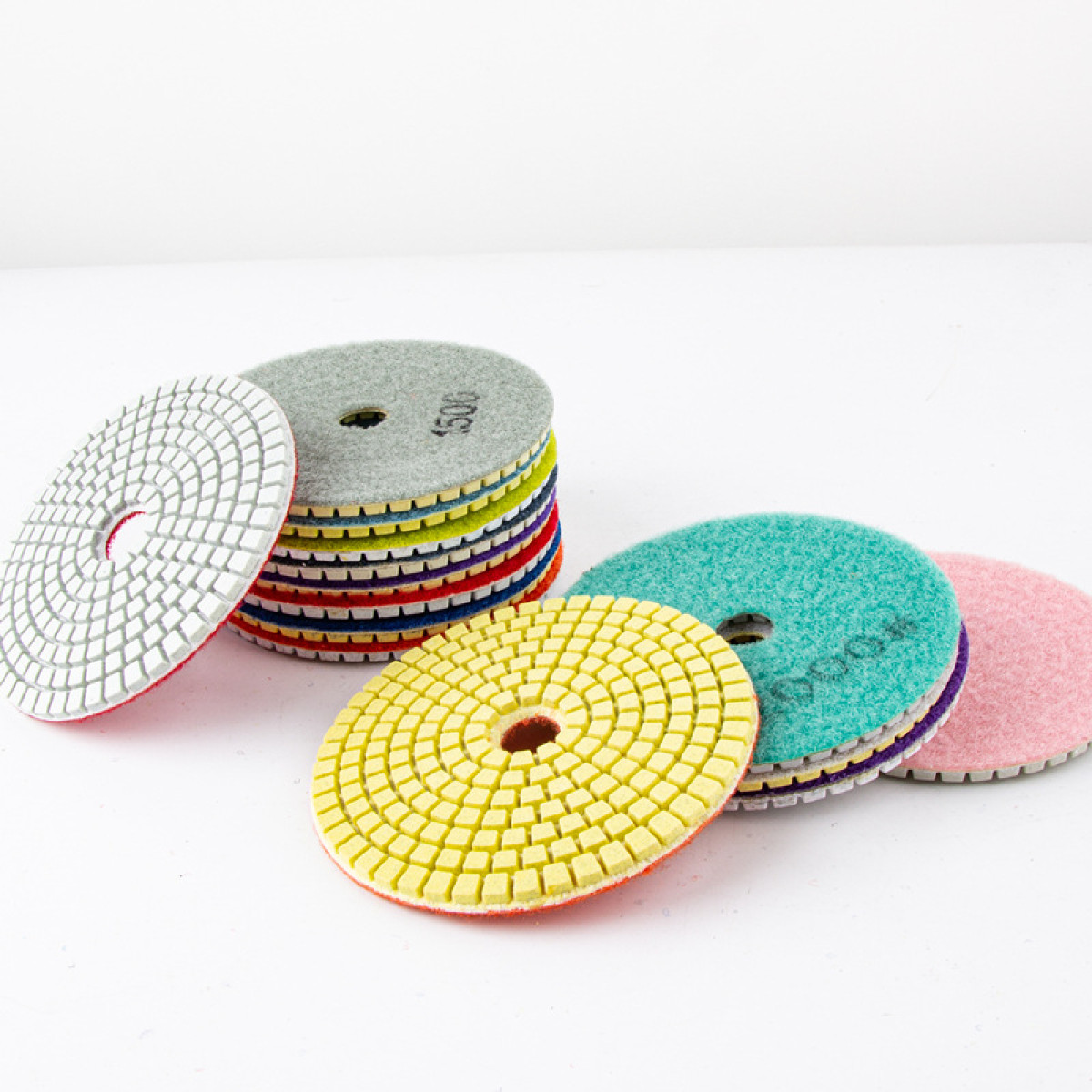 Kilka okrągłych padów polerskich w różnych kolorach na białym tle.